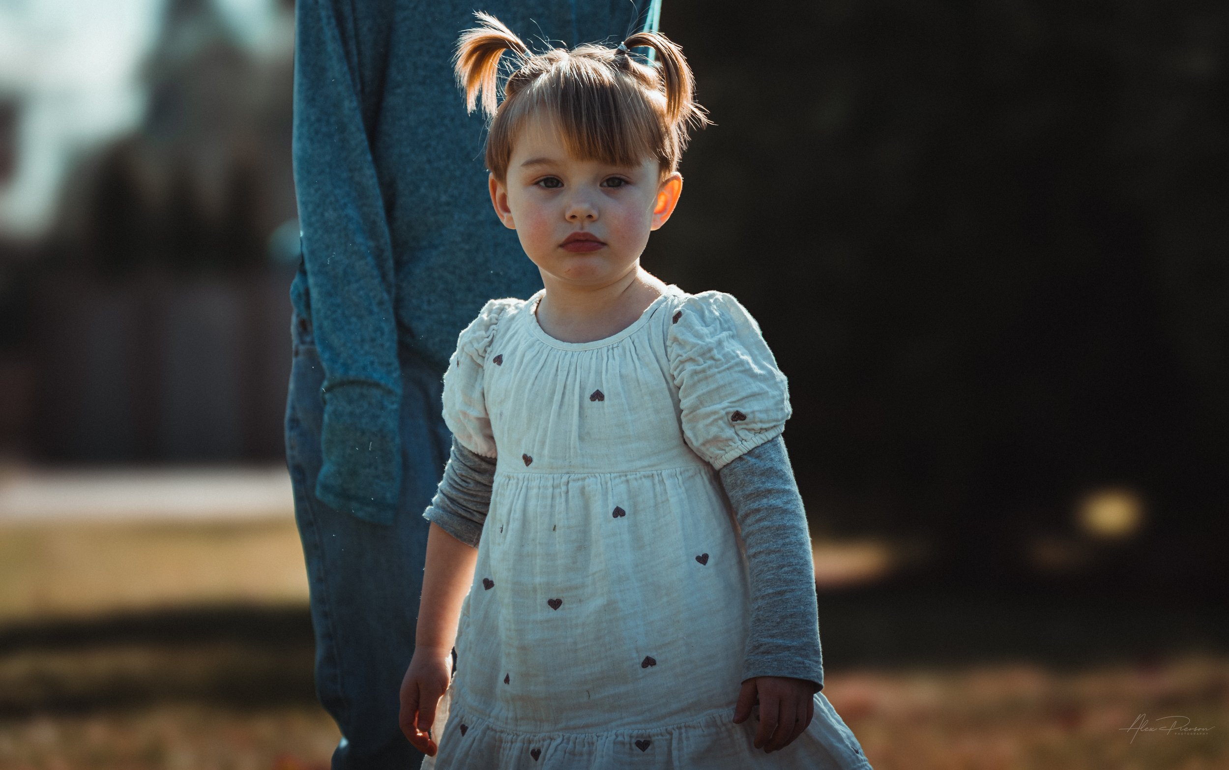  Little girl in white dress stares at the camera with her cousin standing in the back ground during a family photo session in Tumwater, WA – Pacific Northwest lifestyle family and children's photography.