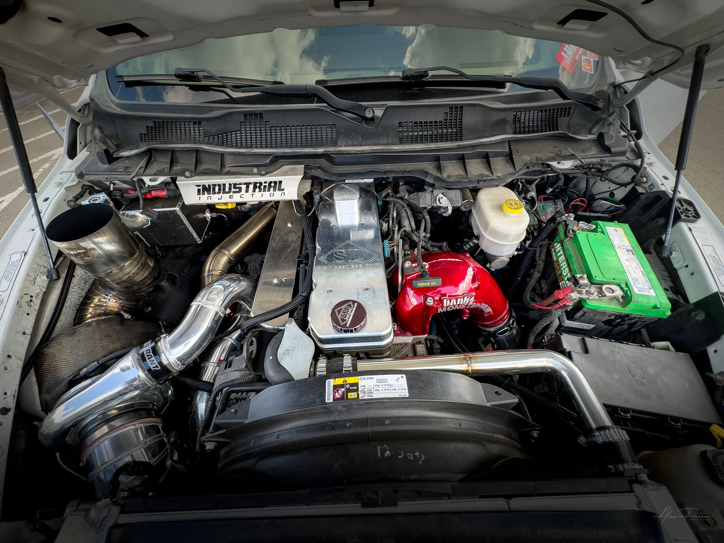 Comprehensive top-down view of a fully built Ram 2500 Cummins diesel engine featuring a Stainless Diesel billet valve cover, Banks intake, and a FUSE hood stack exhaust.
 Fully built Cummins, 6.7 Cummins engine bay, Stainless Diesel valve cover, Cumm