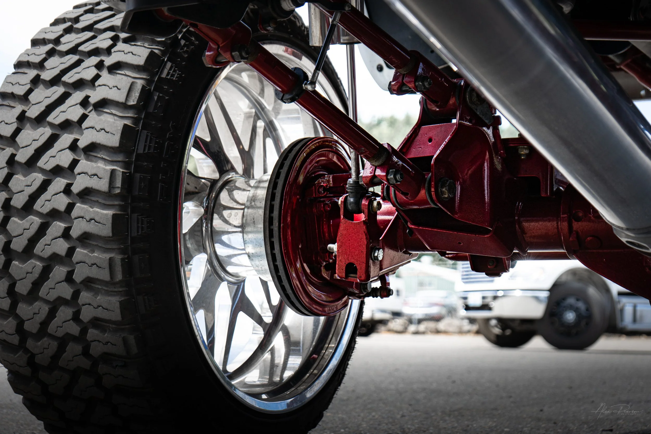 Close-up underneath a lifted Ram 2500 showing a beautifully detailed candy red powder-coated steering knuckle, upgraded brake rotor, and the polished inner wheel barrel.
Red steering knuckle, truck brake rotor, painted suspension parts, custom truck 