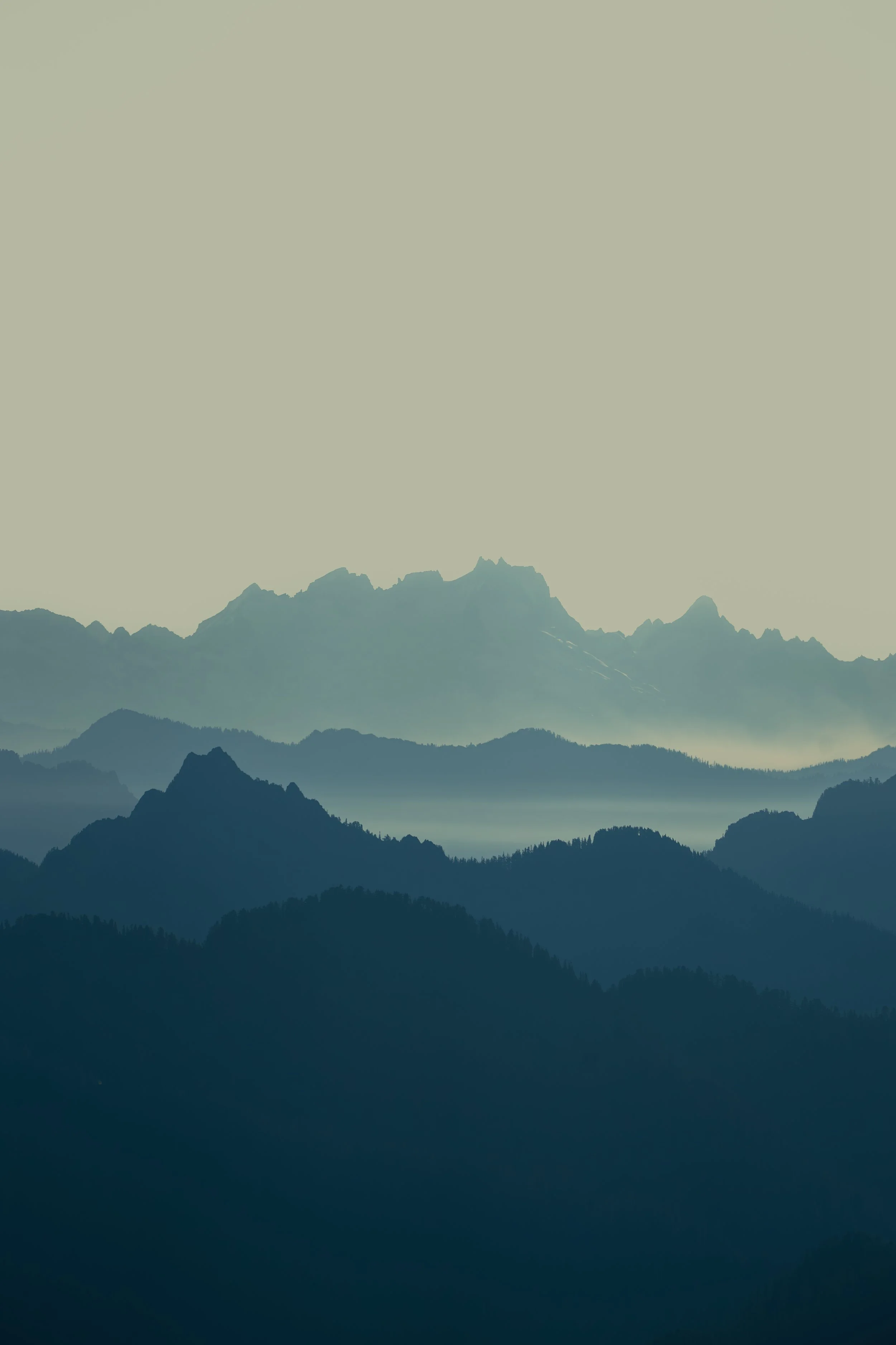 Hazy, blue layered mountain ridges fading into the distance in the Washington Cascades.
 A minimalist study of the hazy, blue mountain ridges of the Cascade Range rolling endlessly into the distance from the Mount Pilchuck viewpoint.
