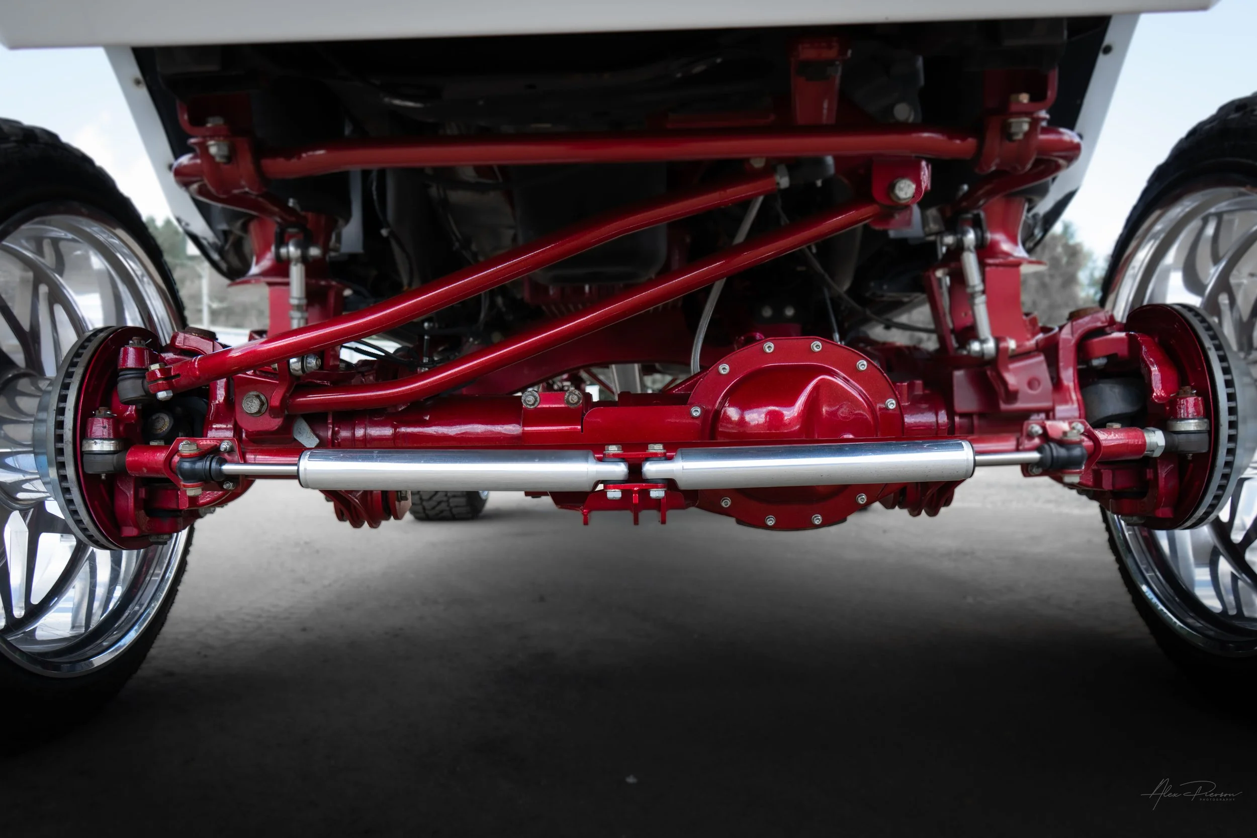 Straight-on view beneath a customized Ram 2500 showcasing the Kelderman air suspension front end, a candy red differential cover, and dual polished steering stabilizers.
Dual steering stabilizer, red front axle, Ram 2500 front suspension, Kelderman l