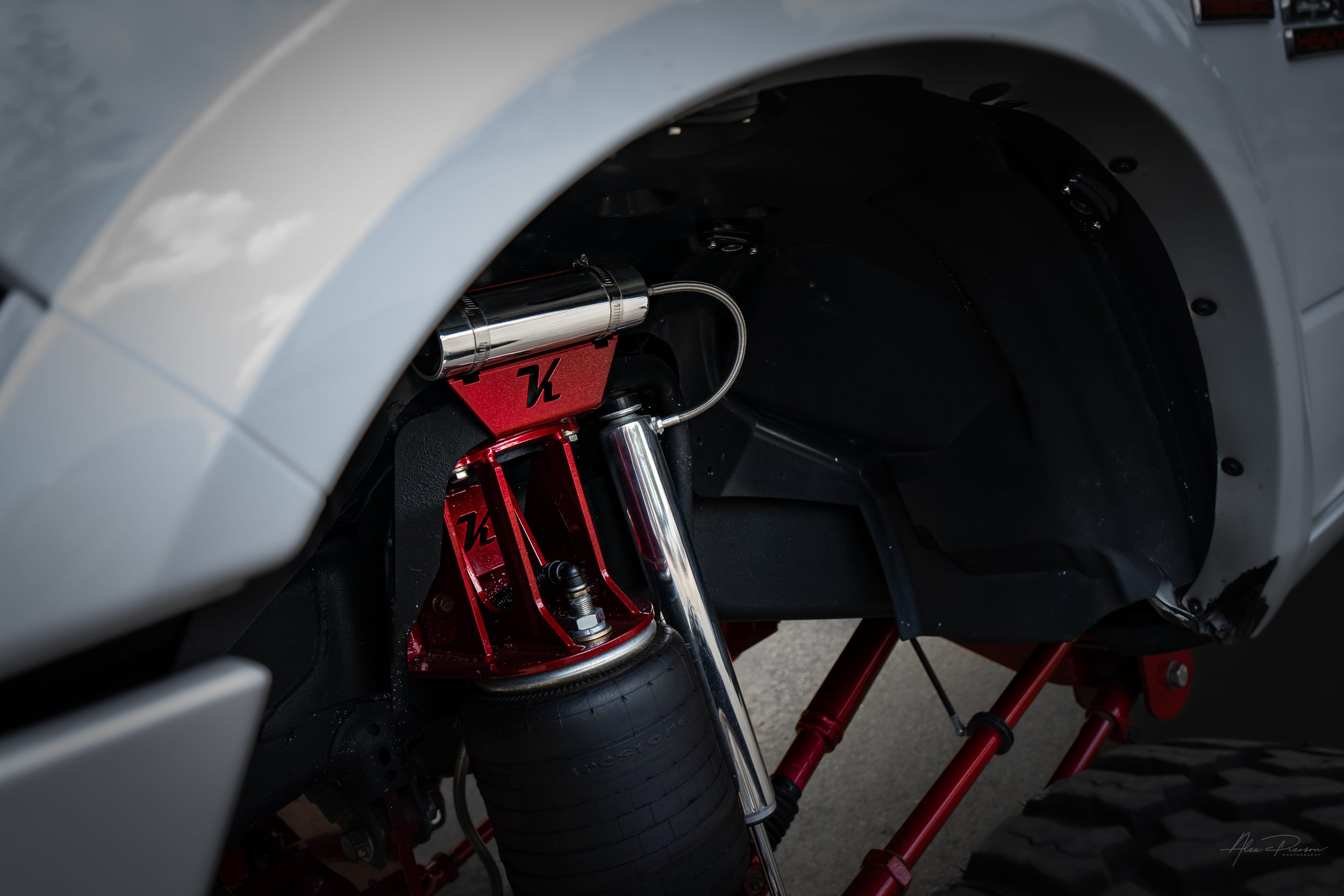 Detail shot of a custom red Kelderman air suspension setup on a lifted Ram 2500, featuring heavy-duty airbags, fabricated brackets with the K logo, and polished shocks.
Kelderman air suspension, front truck airbag, red suspension brackets, polished t