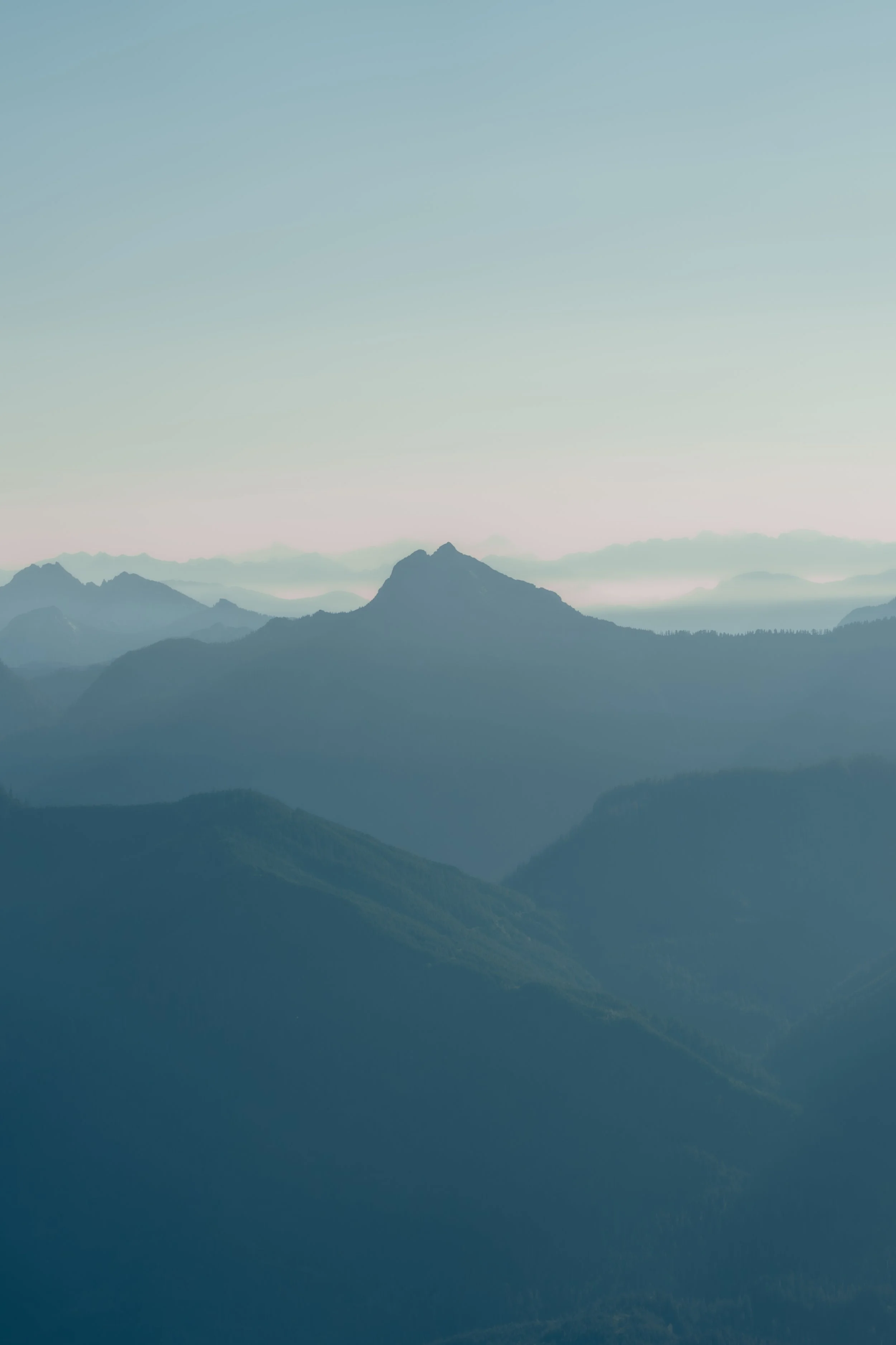 Silhouettes of jagged mountain peaks and misty valleys in shades of blue and grey.
Low-hanging mist settles into the deep valleys between jagged, layered mountain silhouettes, captured from the high vantage point of the Mount Pilchuck lookout.