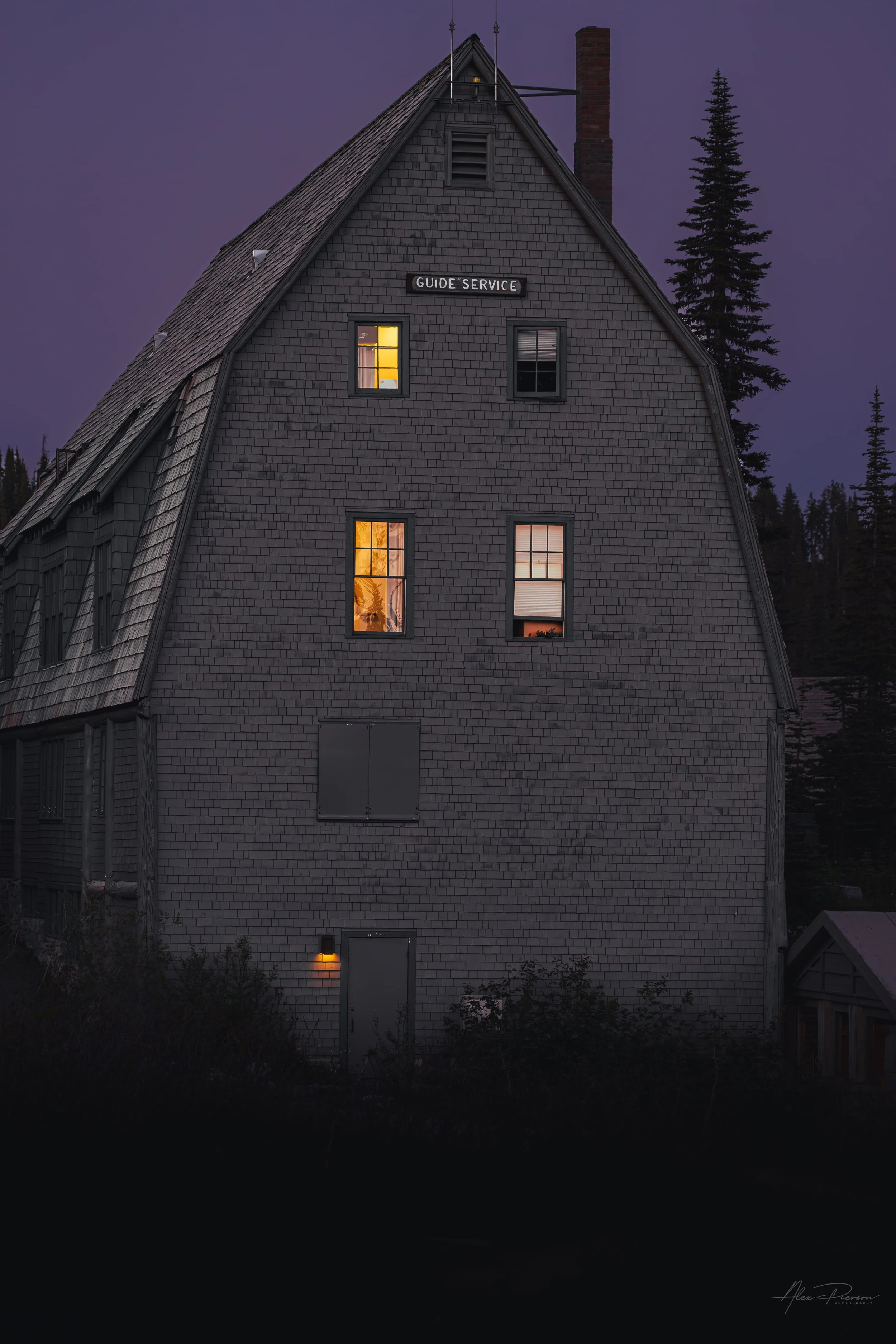 Historic shingled Guide Service building with glowing windows under a purple twilight sky at Mt. Rainier.
The historic, shingle-sided Guide Service building at Mount Rainier glows warmly against a striking deep purple twilight sky in the high alpine 