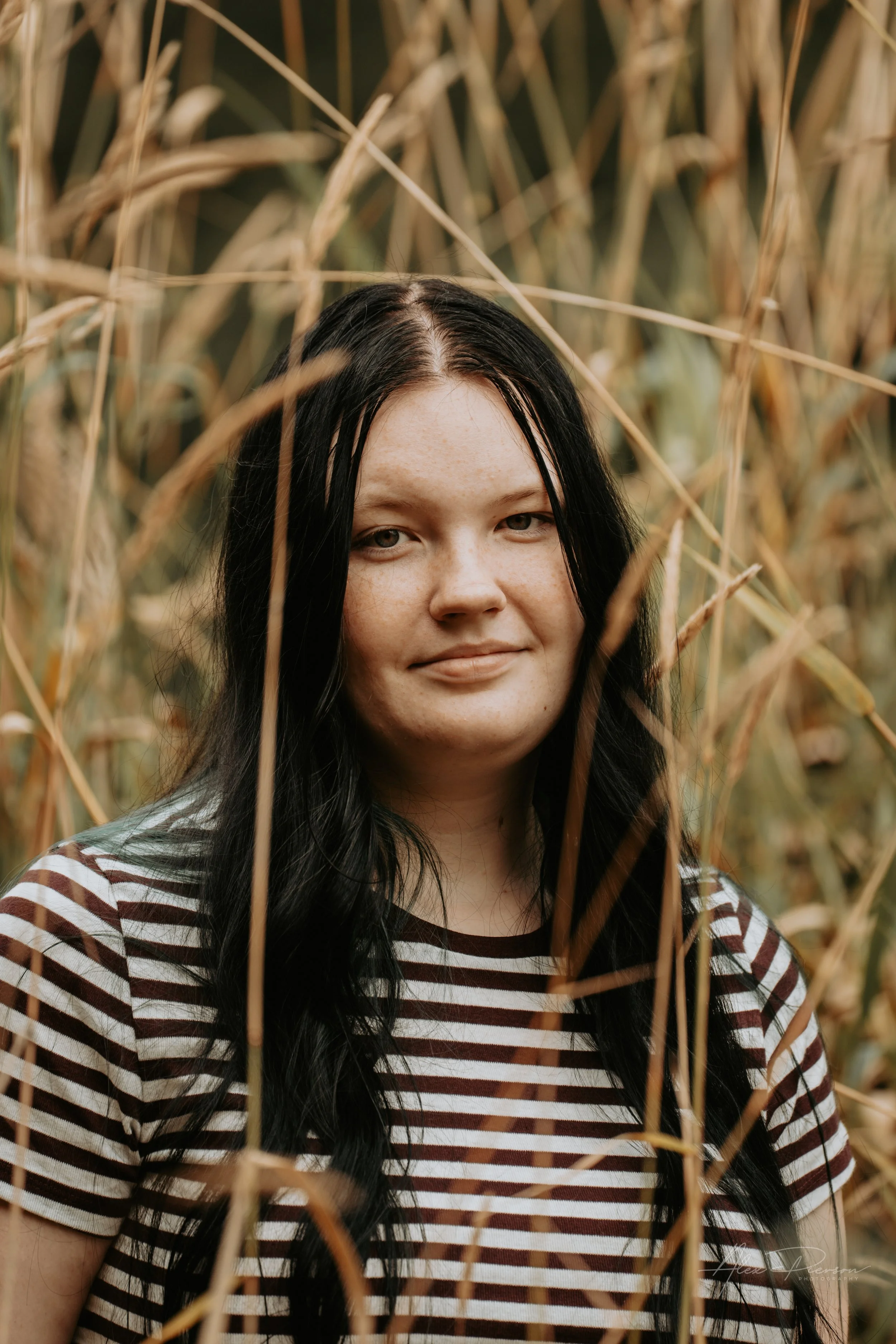 An up close portrait of a young lady wearing a black and white striped shirt, standing in tall dead grass during a family photoshoot in Montesano, WA- – Pacific Northwest lifestyle family and children's photography.
