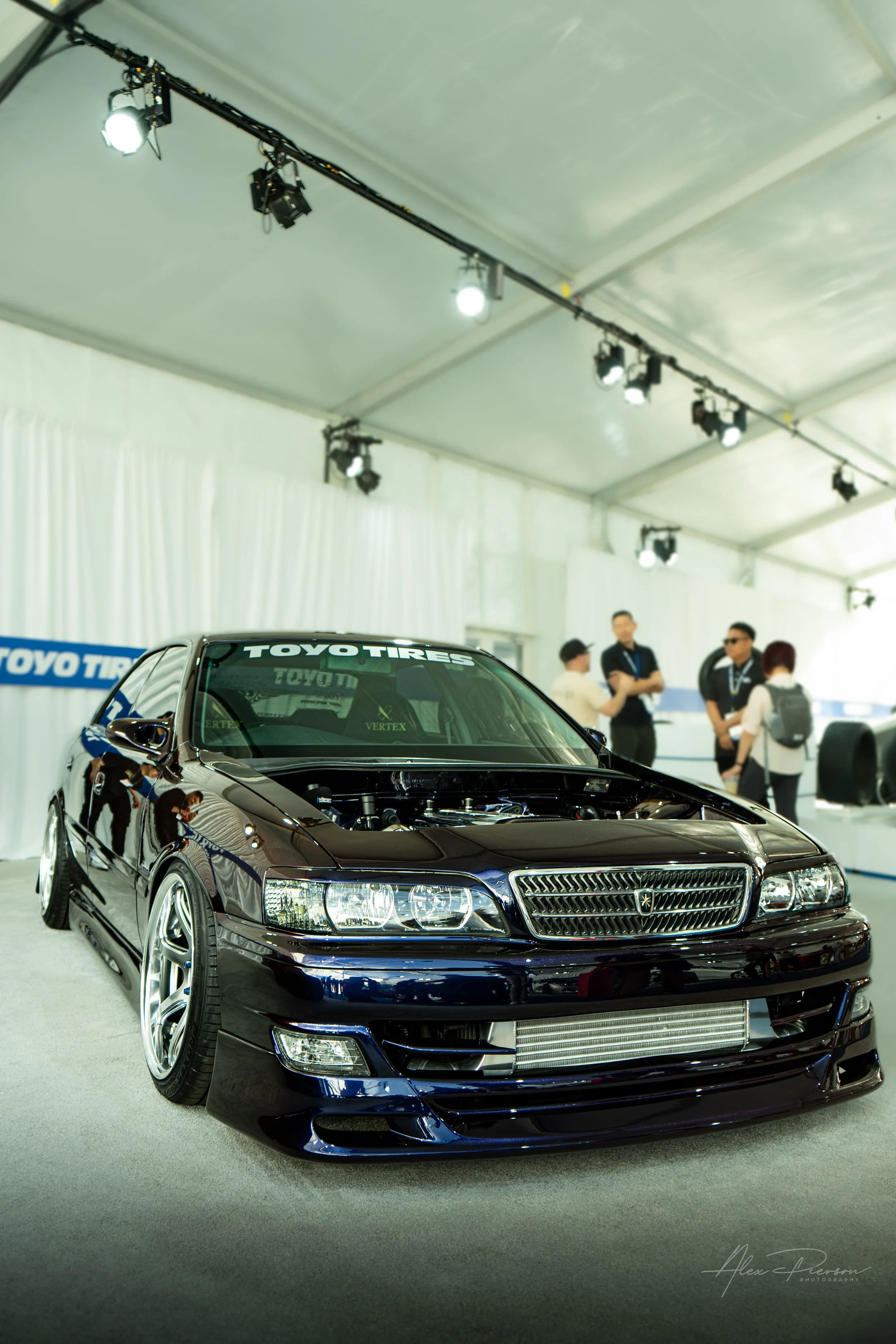 Stanced dark purple Toyota Chaser JZX100 with its hood removed to show a custom engine bay at SEMA.
Flawless JDM execution. A beautifully painted dark purple Toyota Chaser sits flawlessly stanced in the Toyo Tires treadpass, hood removed to show off 