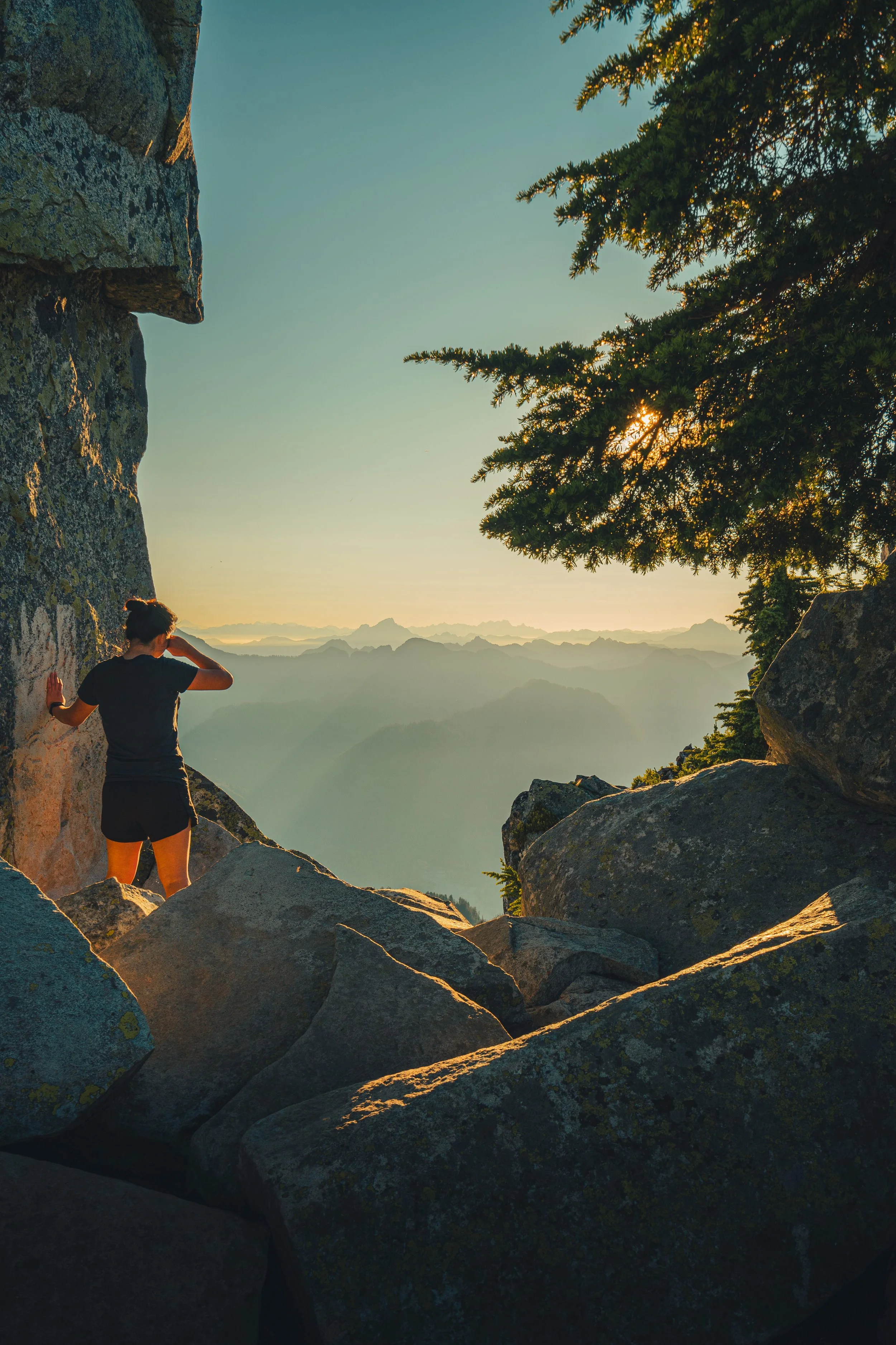 A hiker stands among large granite rocks looking out over a hazy mountain range at sunset on Mt Pilchuck.
Taking in the vast, layered views of the North Cascades. A hiker pauses among the massive granite boulders near the Mount Pilchuck summit as the