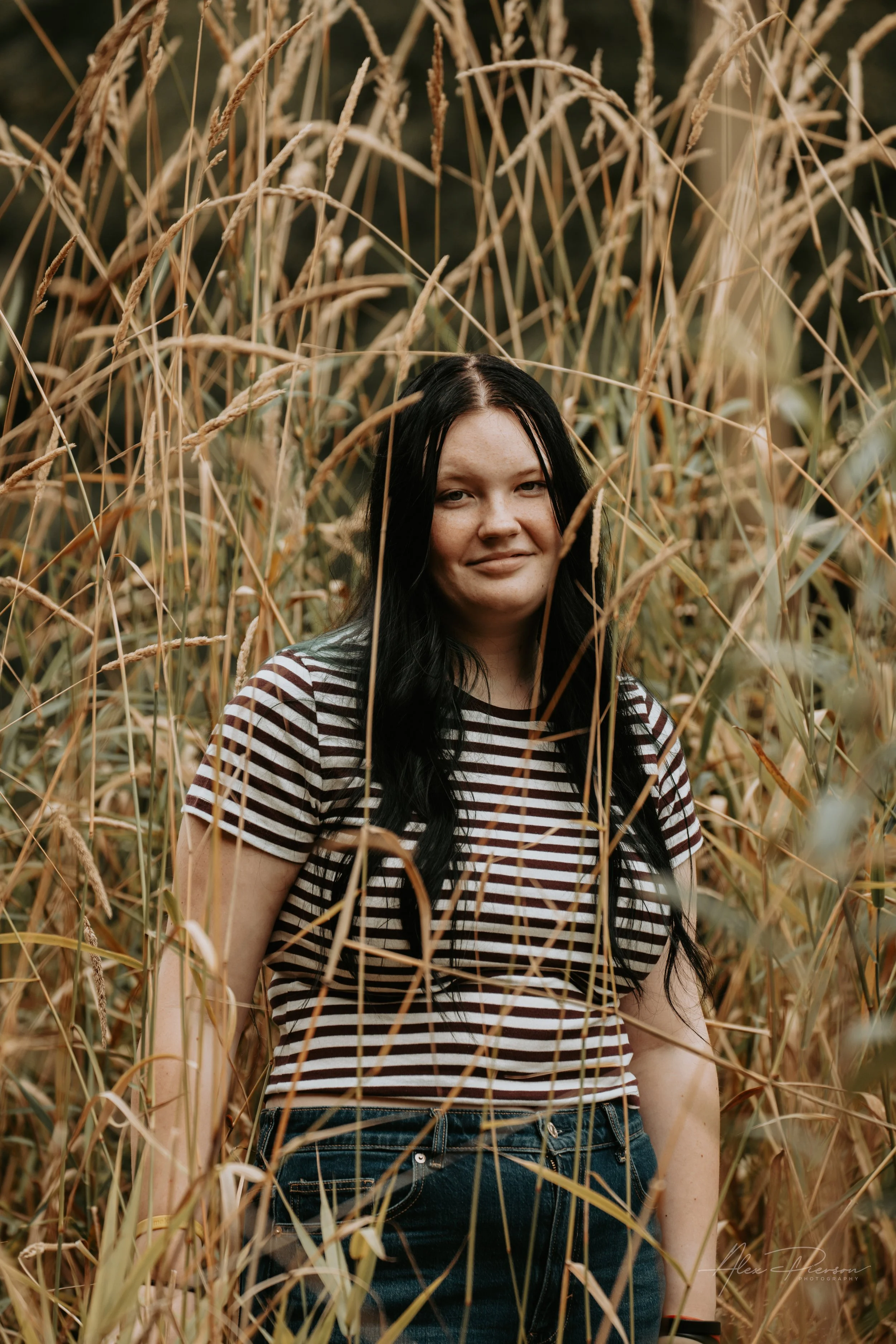 An up close portrait of a young lady wearing a black and white striped shirt, standing in tall dead grass during a family photoshoot in Montesano, WA- – Pacific Northwest lifestyle family and children's photography.