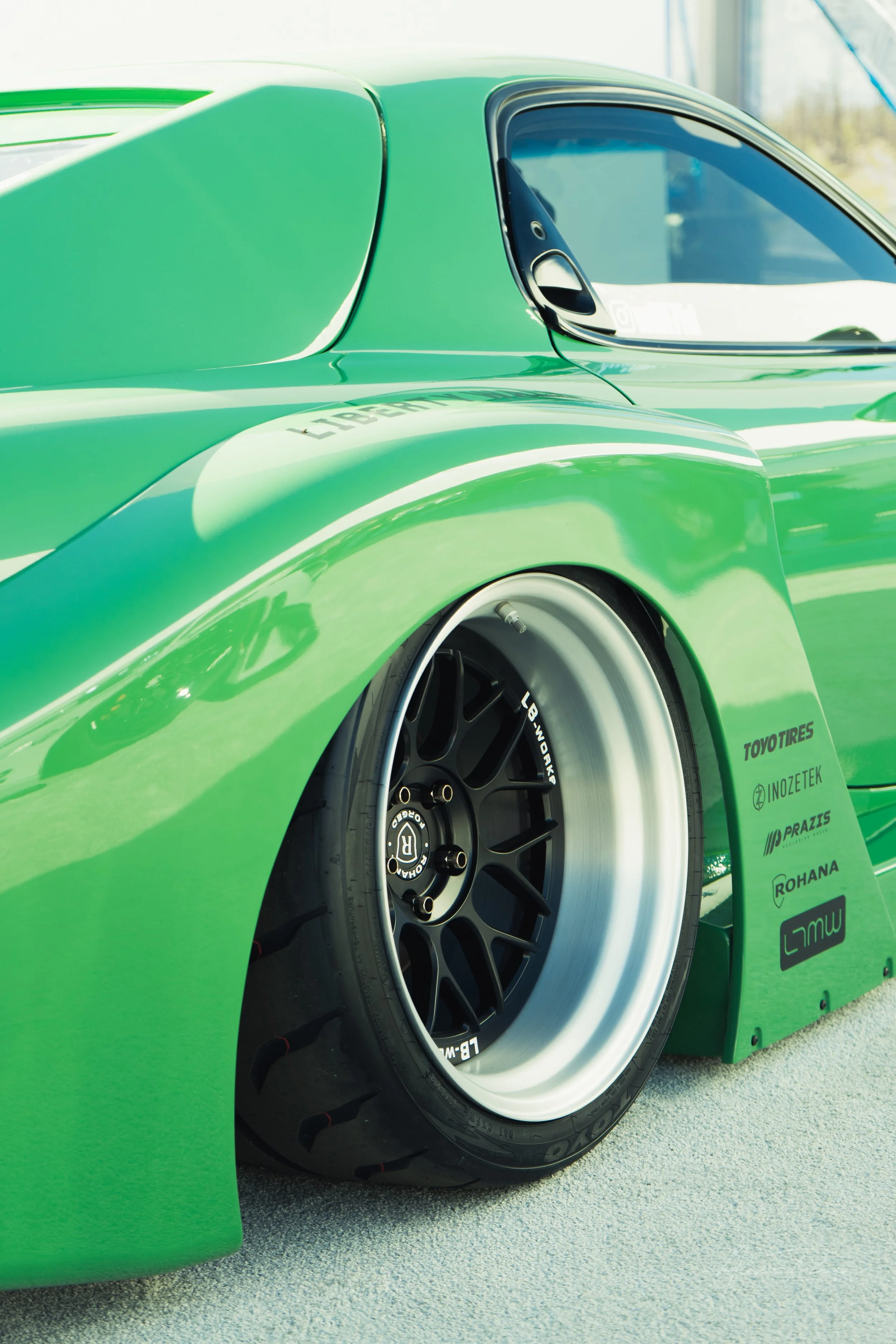 Close up of deep dish wheels tucked under green Liberty Walk widebody fenders on a Mazda RX-7 at SEMA.
Flawless fitment. A close-up look at the aggressive deep-dish wheels tucked perfectly under the massive green Liberty Walk overfenders of this cust