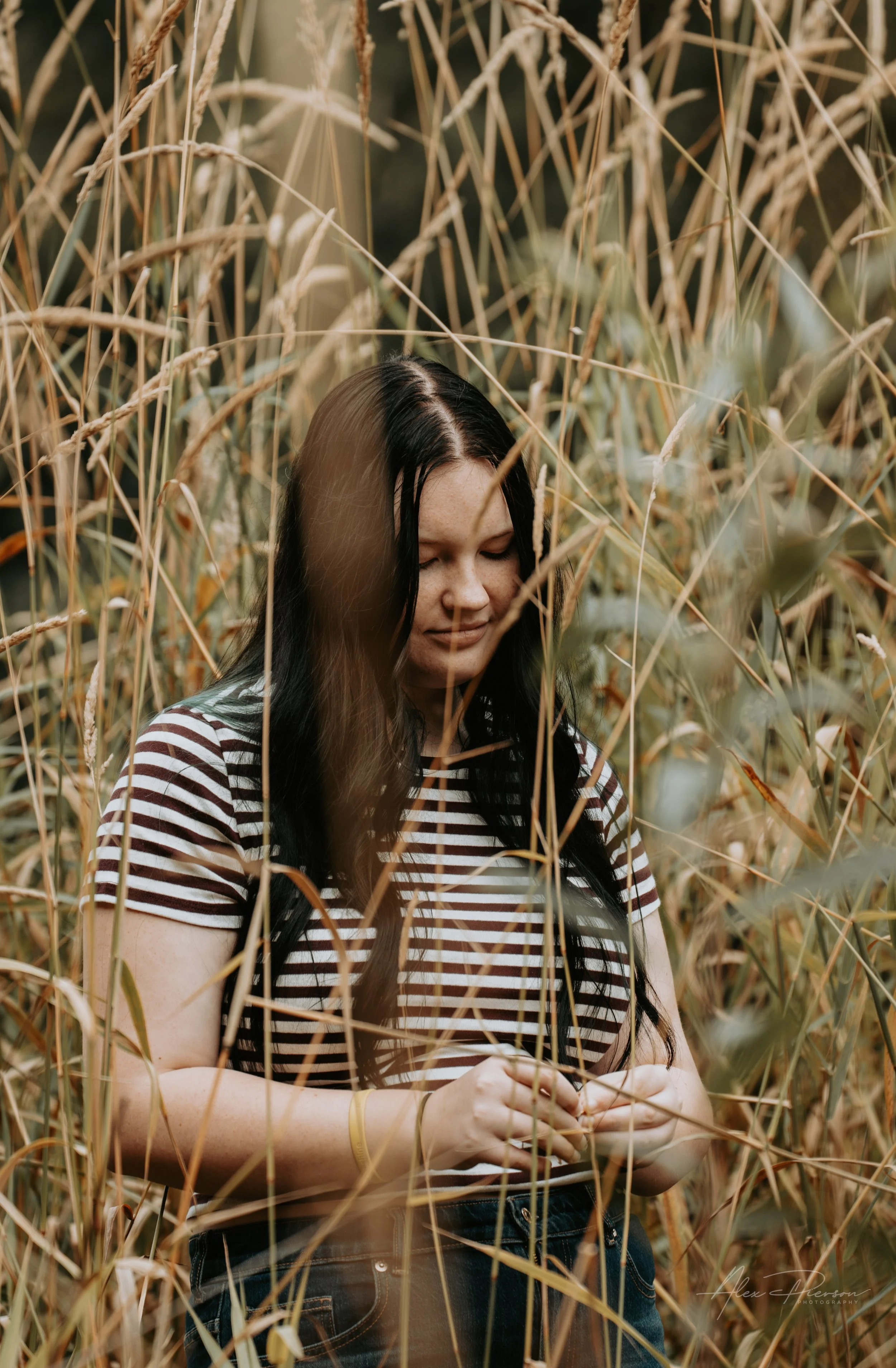 An up close portrait of a young lady wearing a black and white striped shirt, standing in tall dead grass during a family photoshoot in Montesano, WA- – Pacific Northwest lifestyle family and children's photography.