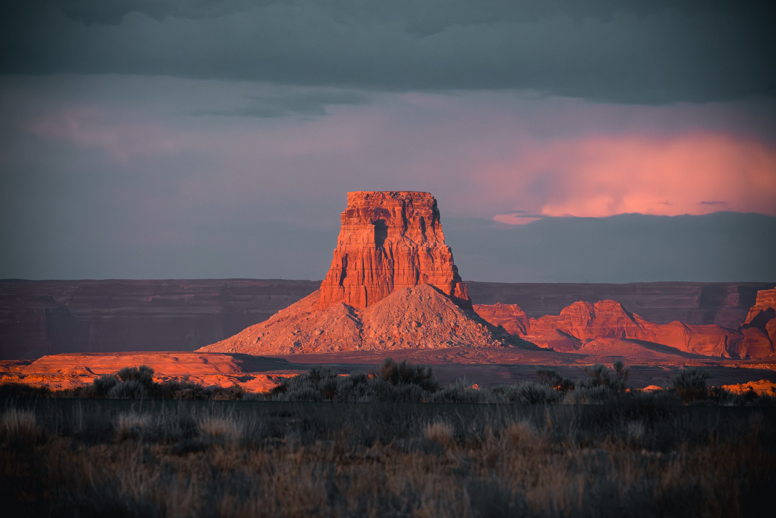 A towering red rock butte in Page, Arizona glowing brightly against a dark, stormy desert sky.
The dramatic contrasts of the American Southwest. A towering red rock butte in Page, Arizona, catches the intense, fiery light of the setting sun against a