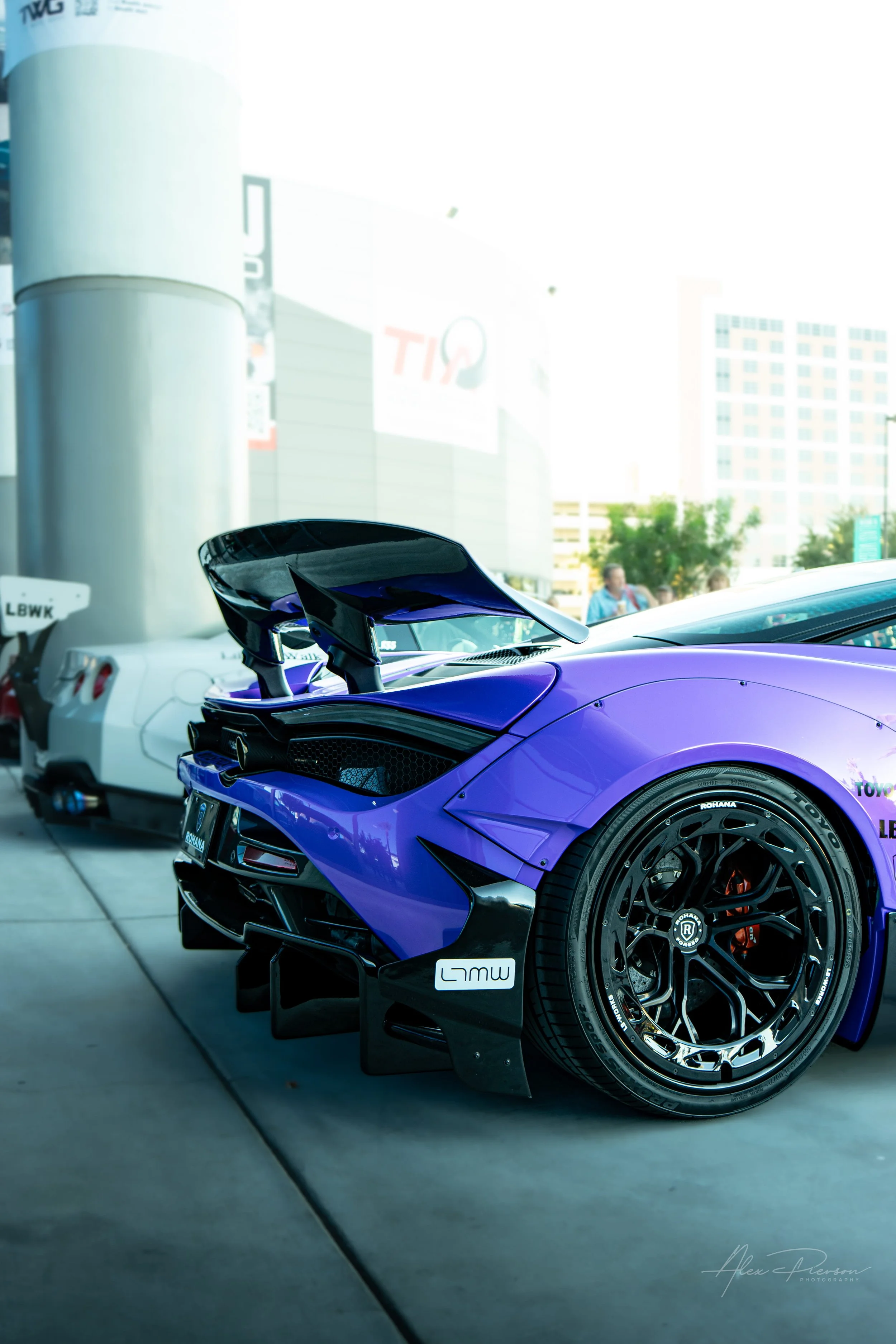 Rear view of a stanced Liberty Walk wide body purple McLaren showing a massive carbon fiber wing and custom aerodynamic diffuser at SEMA.
Aggressive aerodynamics on full display. This custom purple McLaren turns heads with a massive rear wing, flared