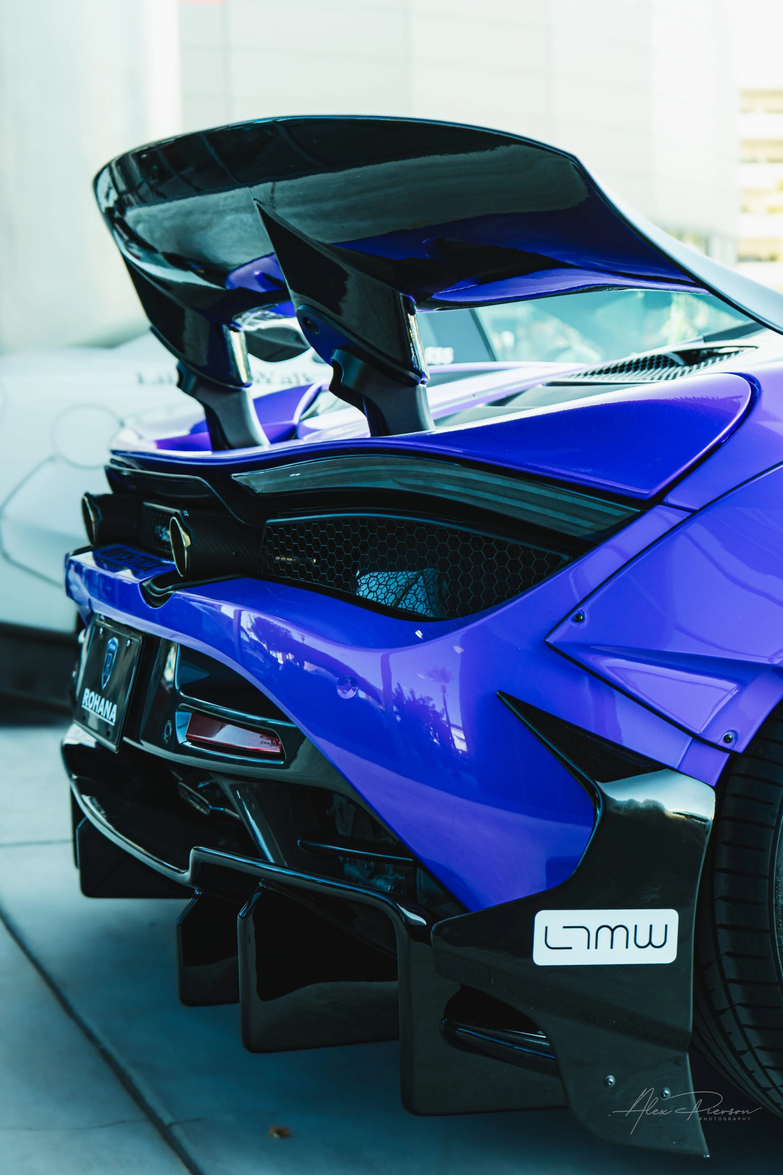 A more close up rear view of a stanced Liberty Walk wide body purple McLaren showing a massive carbon fiber wing and custom aerodynamic diffuser at SEMA.
Aggressive aerodynamics on full display. This custom purple McLaren turns heads with a massive r
