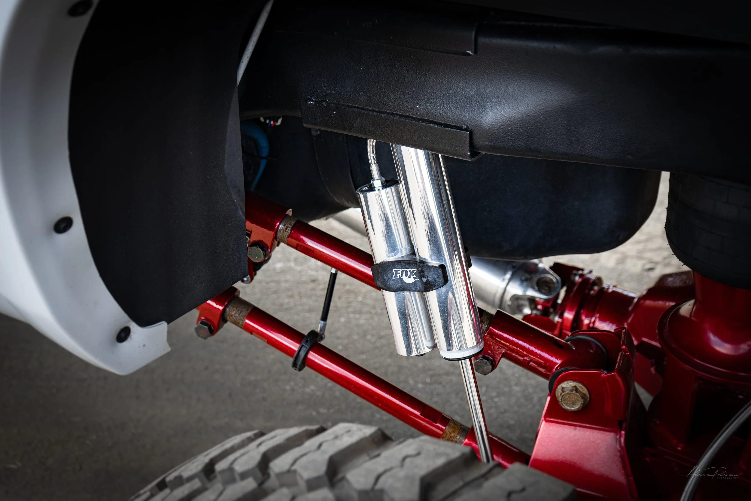 Detailed view of the rear Kelderman air suspension on a custom Ram 2500 featuring polished Fox remote reservoir shocks and red powder-coated trailing arms.
Fox shocks, Kelderman air ride, lifted truck suspension, Ram 2500 air suspension.
polished Fox