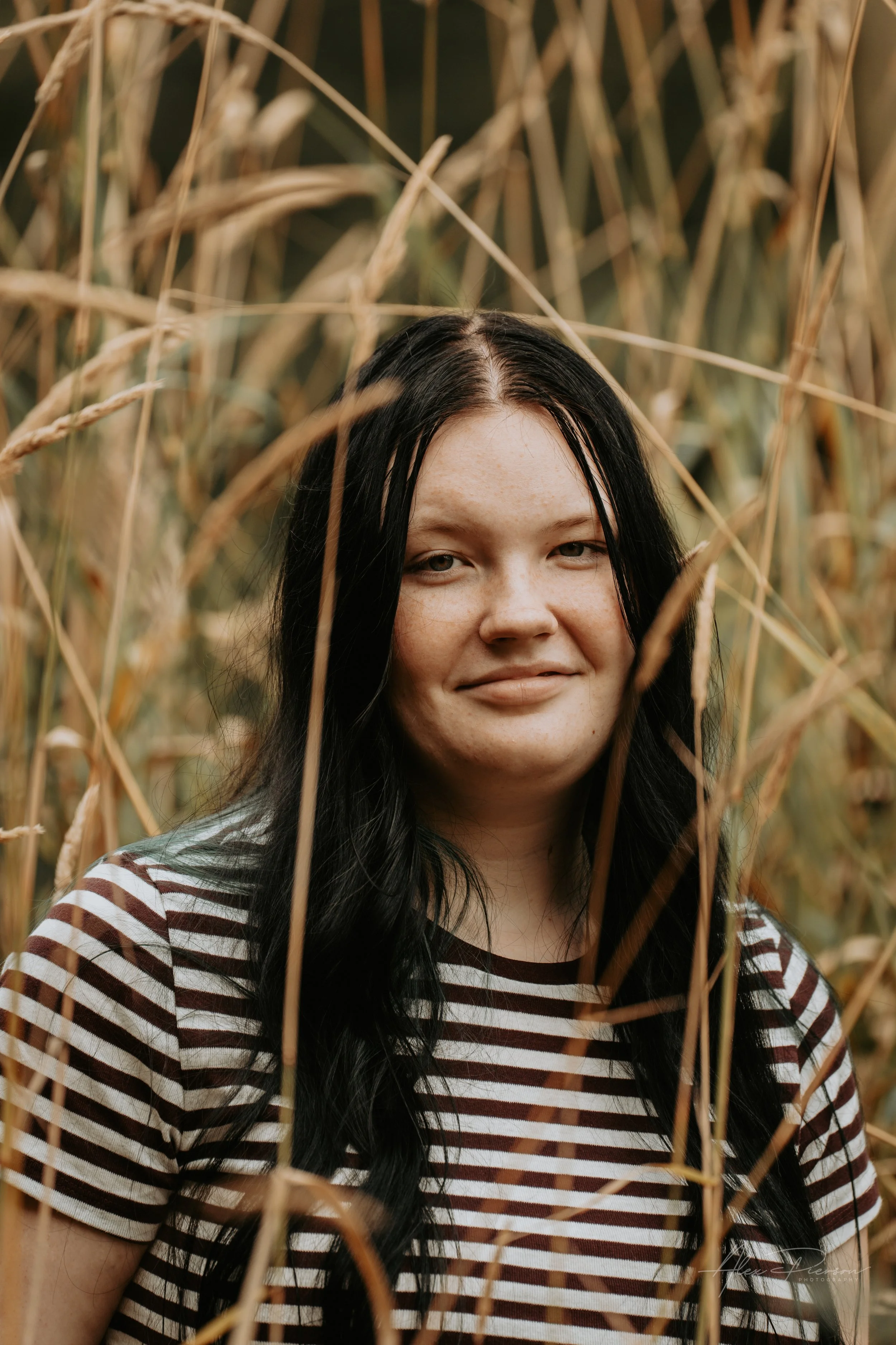 An up close portrait of a young lady wearing a black and white striped shirt, standing in tall dead grass during a family photoshoot in Montesano, WA- – Pacific Northwest lifestyle family and children's photography.