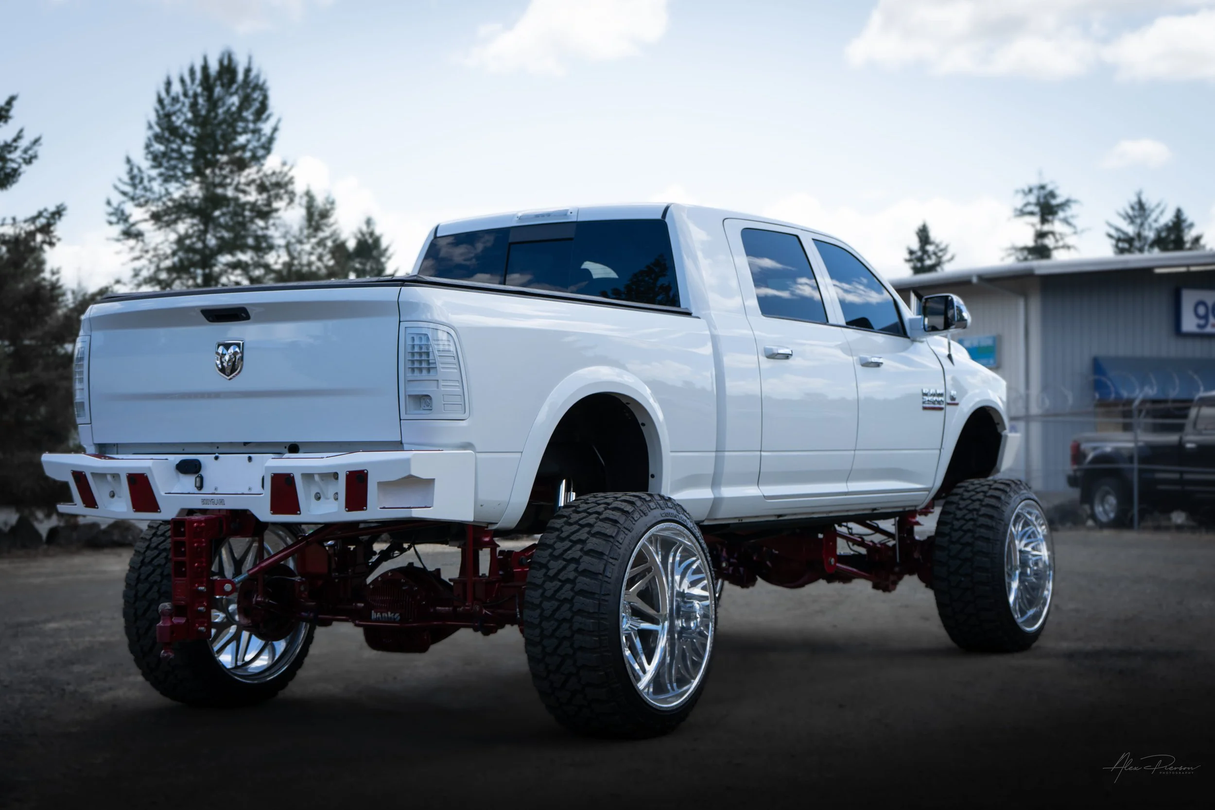 Rear 3/4 view of a show-quality white Ram 2500 showcasing a custom Bodyguard rear bumper, adjustable drop hitch, and detailed red Kelderman air suspension.
Lifted Ram 2500 rear, Kelderman suspension, heavy duty drop hitch, show truck rear.
rear view 