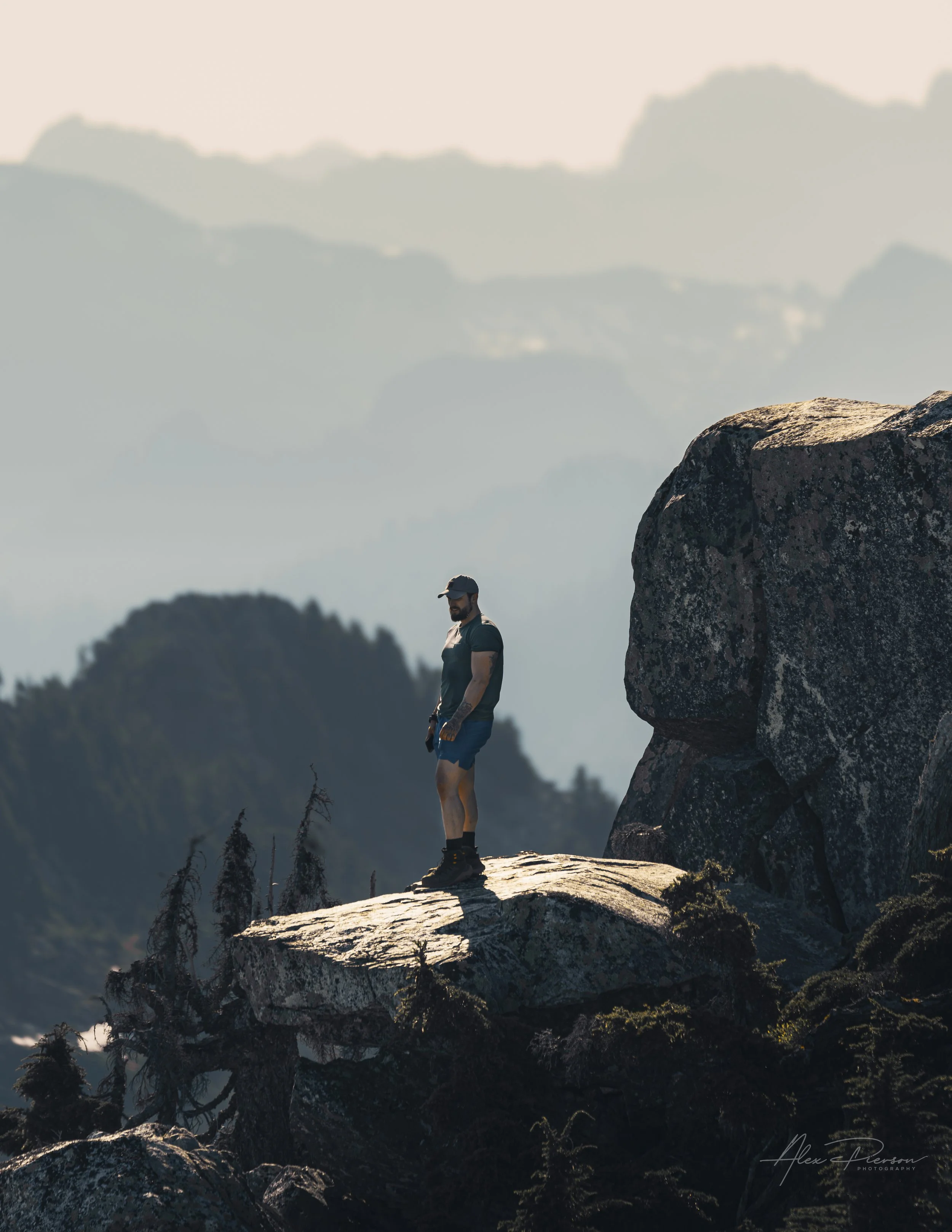 Hiker standing on a dramatic granite ledge looking out at hazy mountain layers at Mount Pilchuck.
A true sense of scale and perspective. A hiker stands on a dramatic granite precipice looking out over the hazy, endless layers of the Washington wilder