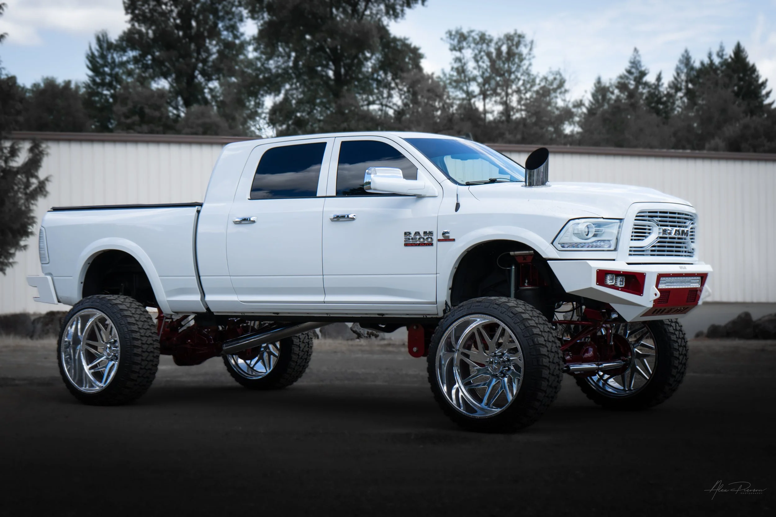 Show-quality lifted white Ram 2500 displaying an aggressive stance, highlighting its red Kelderman air suspension, custom Bodyguard bumpers, and a massive hood stack exhaust.
Lifted Ram 2500 stance, Kelderman show truck, truck hood stack, white Dodge
