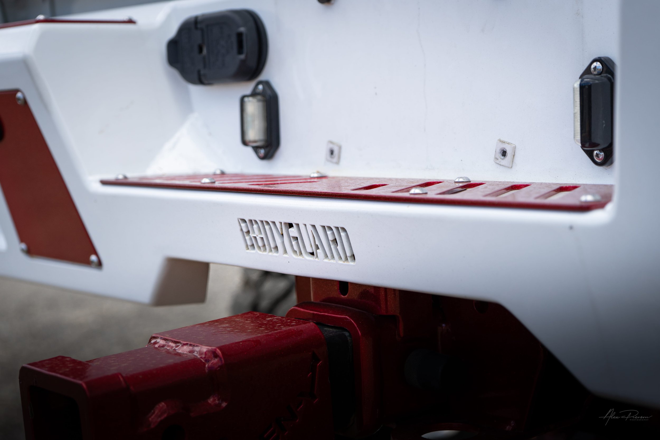 Custom white Bodyguard rear bumper with integrated LED lighting and a heavy-duty candy red adjustable drop hitch on a lifted Ram 2500.
 Adjustable drop hitch, Ram 2500 tow hitch, custom truck hitch, white rear bumper.
heavy-duty adjustable red drop h