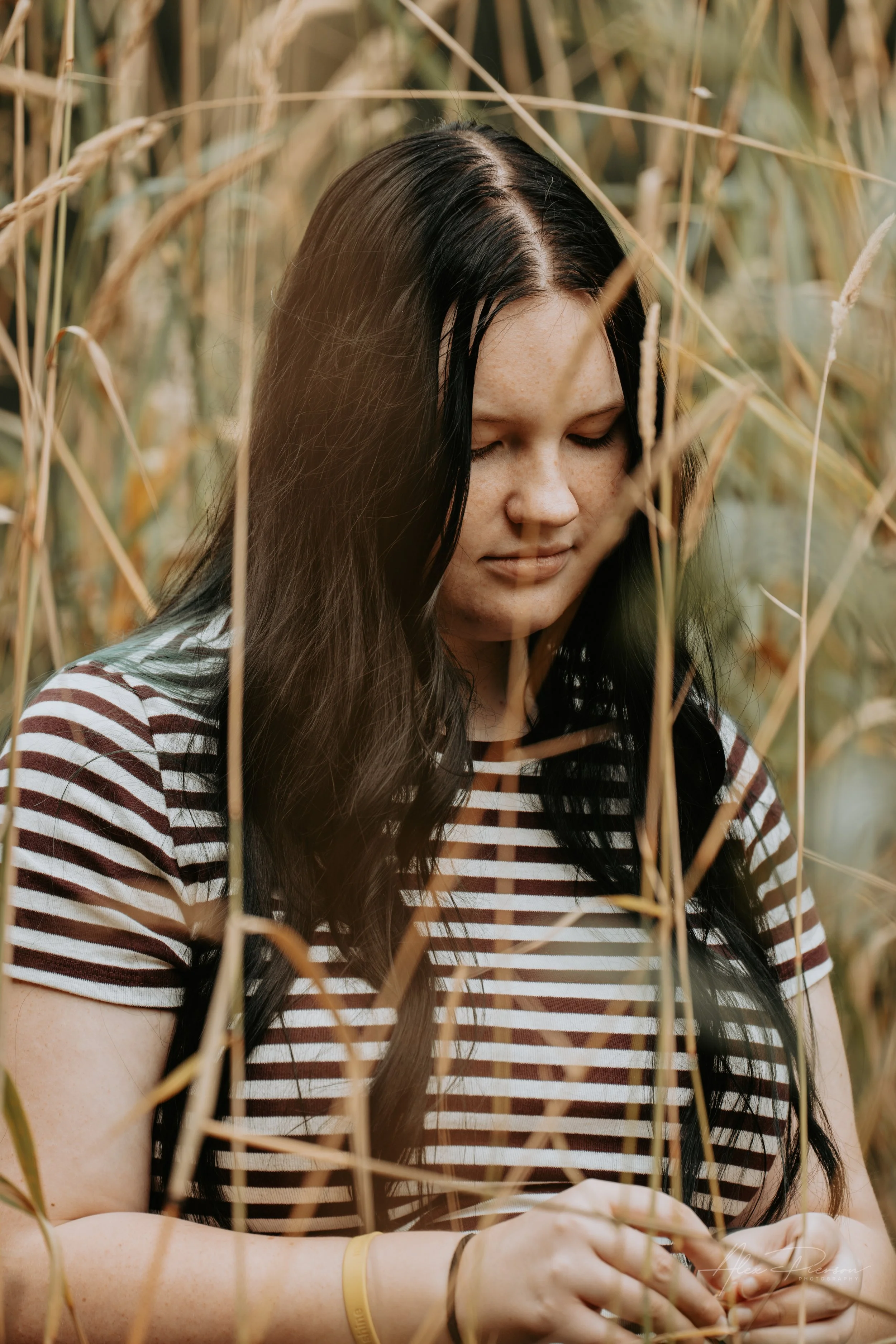 An up close portrait of a young lady wearing a black and white striped shirt, standing in tall dead grass during a family photoshoot in Montesano, WA- – Pacific Northwest lifestyle family and children's photography.