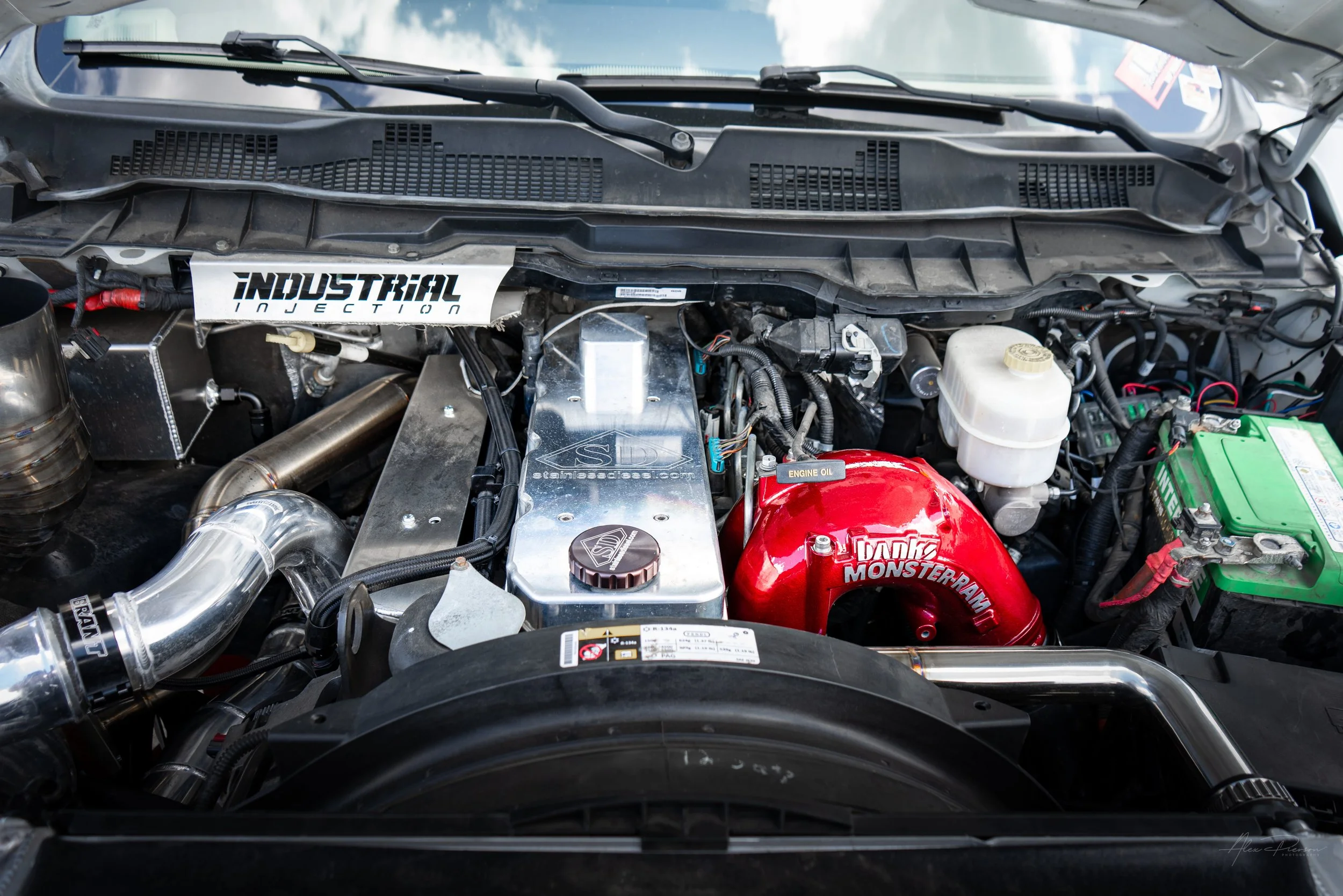 Modified Ram 2500 Cummins diesel engine bay showcasing a polished Stainless Diesel billet valve cover, red Banks Monster-Ram intake, and custom turbo piping.
Stainless Diesel valve cover, Cummins billet cover, Banks Monster Ram, 6.7 Cummins upgrades.