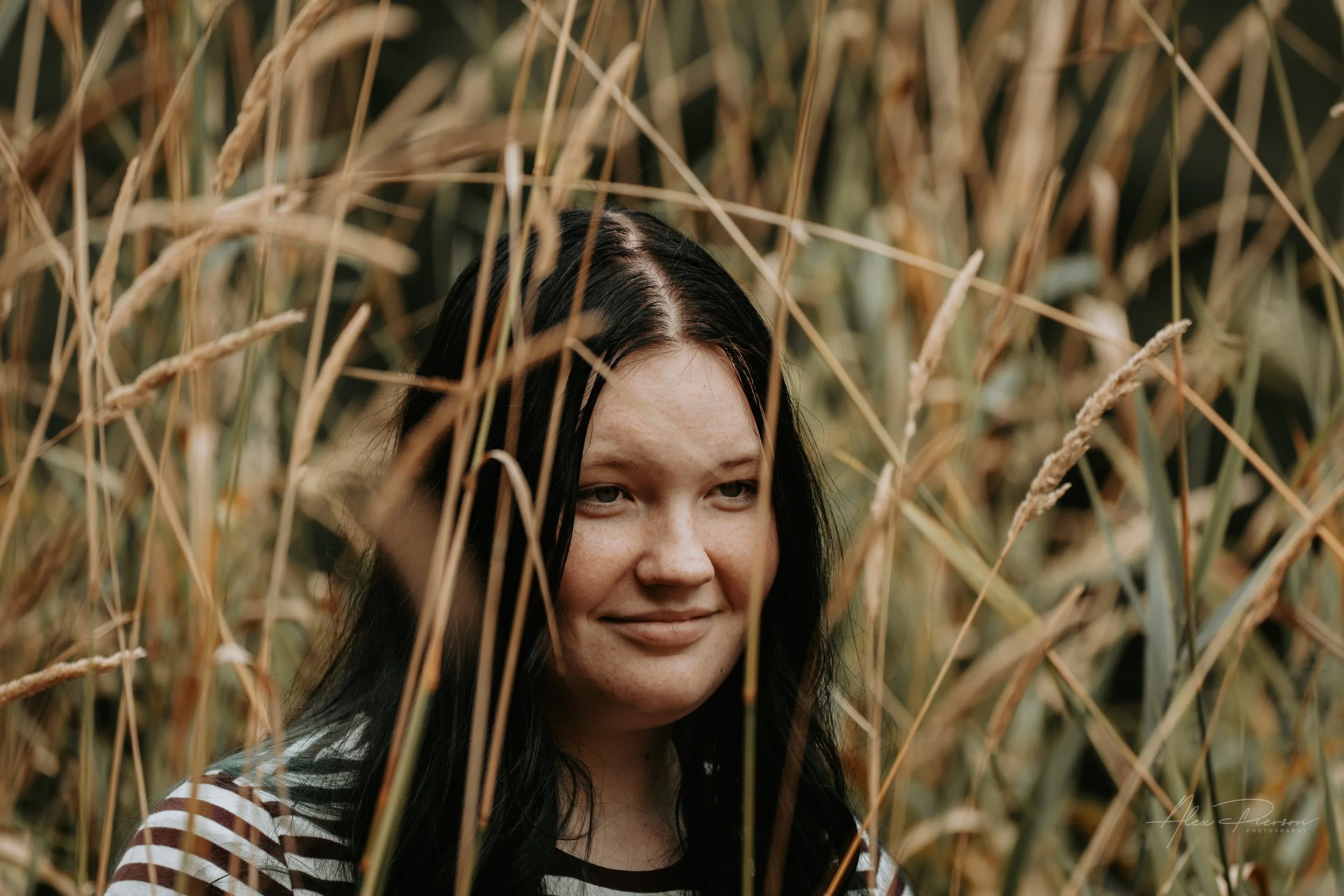 An up close portrait of a young lady wearing a black and white striped shirt, standing in tall dead grass during a family photoshoot in Montesano, WA- – Pacific Northwest lifestyle family and children's photography.