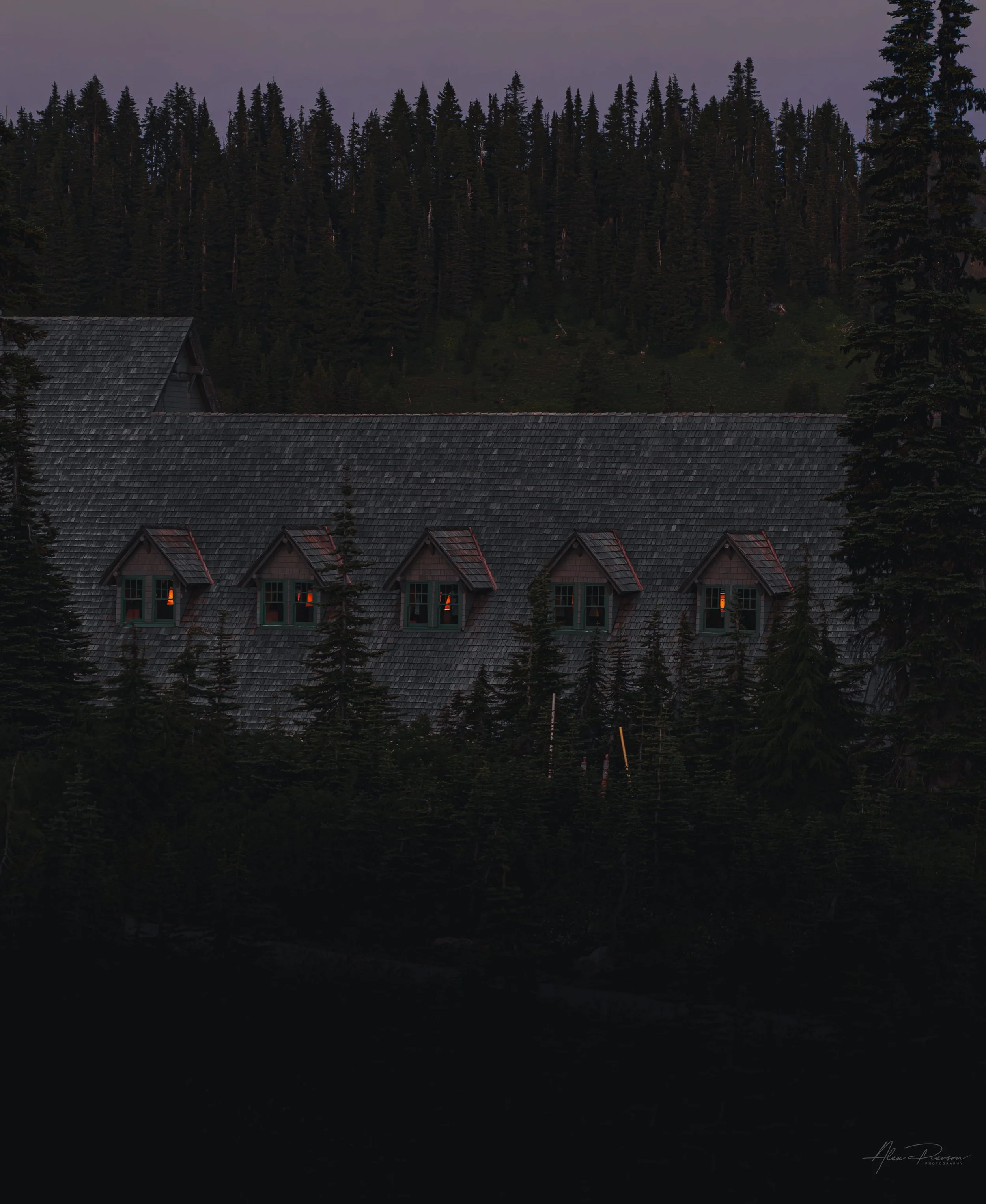 Glowing dormer windows on the historic Paradise Inn roofline at dusk in Mount Rainier National Park.
Warm light spills from the dormer windows of the historic Paradise Inn, offering a cozy contrast to the moody, dark evergreen forest of Mount Rainier