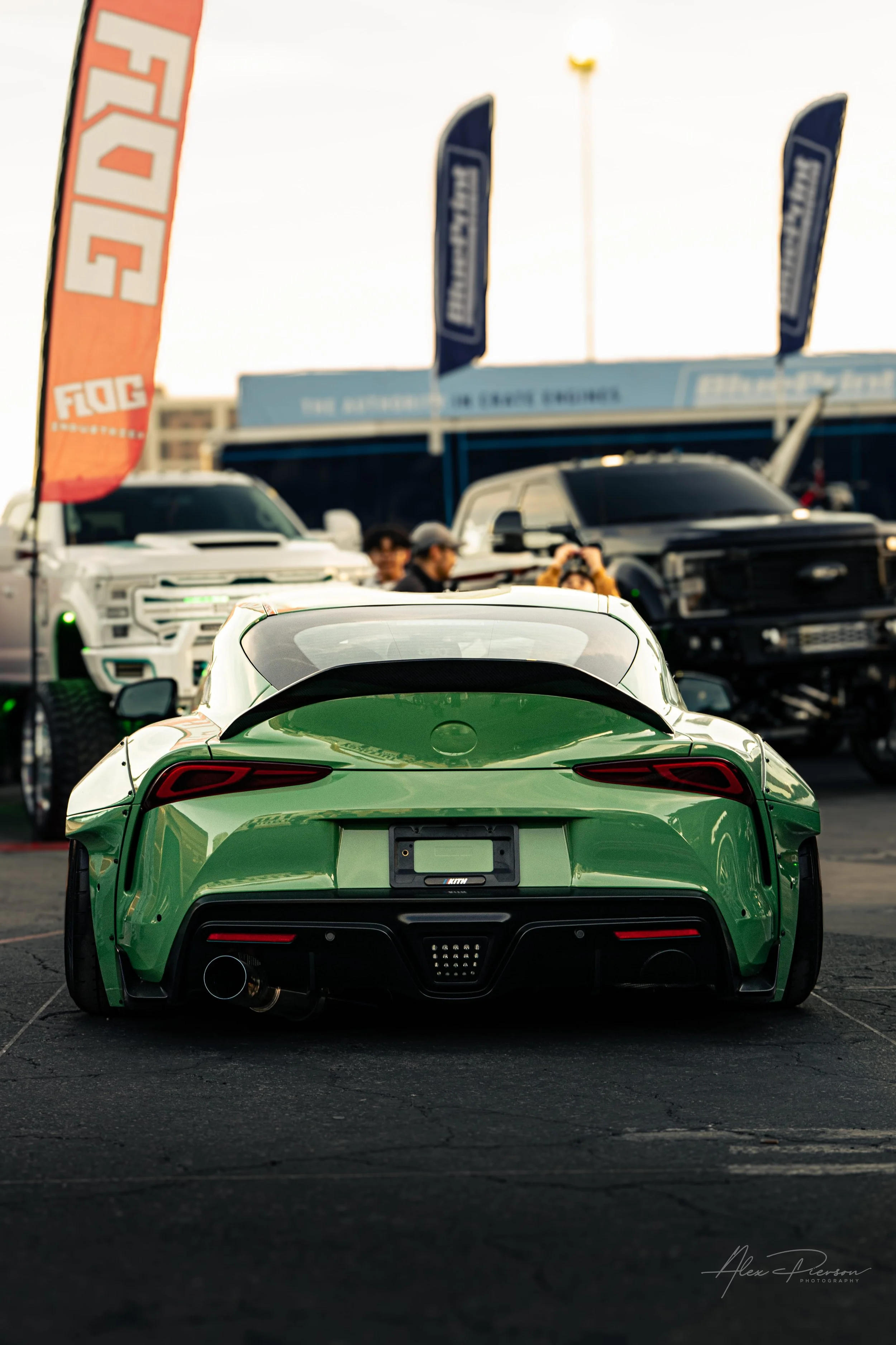 Rear view of a custom stanced green Toyota Supra MK5 with a widebody kit and ducktail spoiler at SEMA.
Unmistakable presence. The widened rear end of a custom green MK5 Toyota Supra featuring a sleek ducktail spoiler and aggressive aftermarket diffus