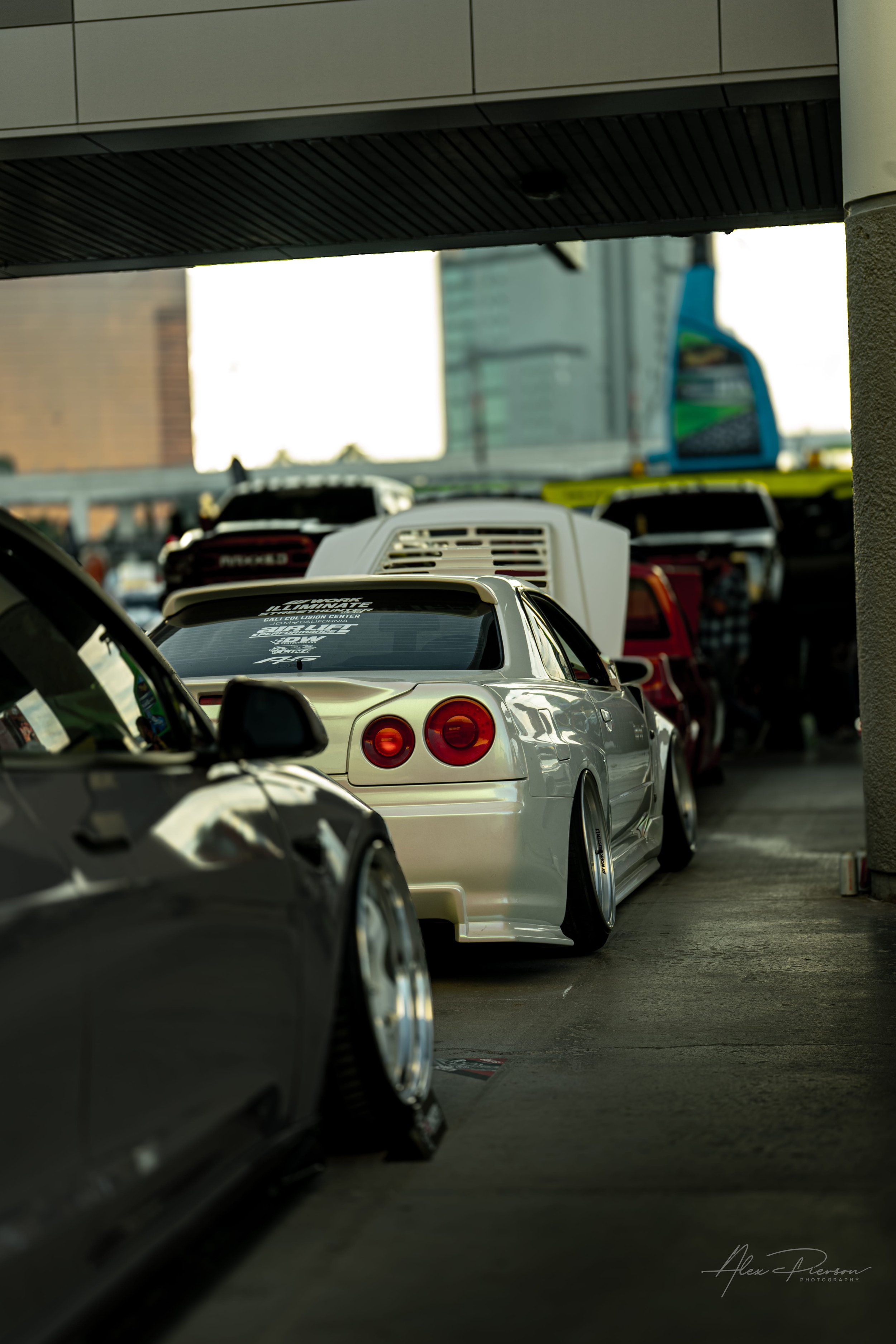 A stanced white Nissan Skyline R34 parked in a line of custom tuner cars at SEMA Las Vegas.
JDM royalty. A beautifully stanced white Nissan Skyline R34 sits low to the ground in a lineup of high-end custom automotive builds at the SEMA Show.