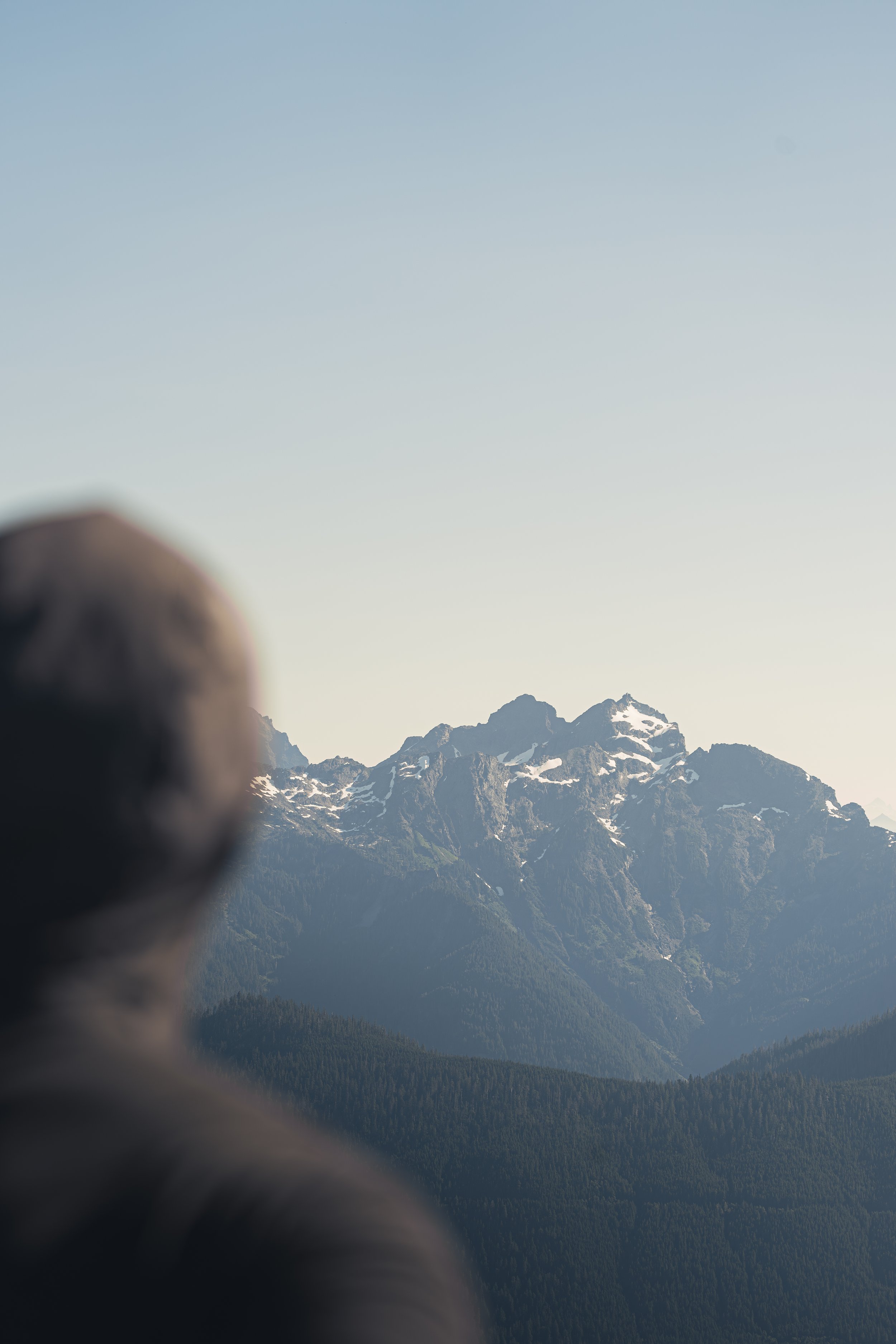 An out-of-focus silhouette of a person looking out at a sharp, snow-dusted mountain peak in the Washington Cascades.
Taking in the rugged beauty of the Washington Cascades. A blurred silhouette in the foreground frames a stunning, sharp snow-capped p