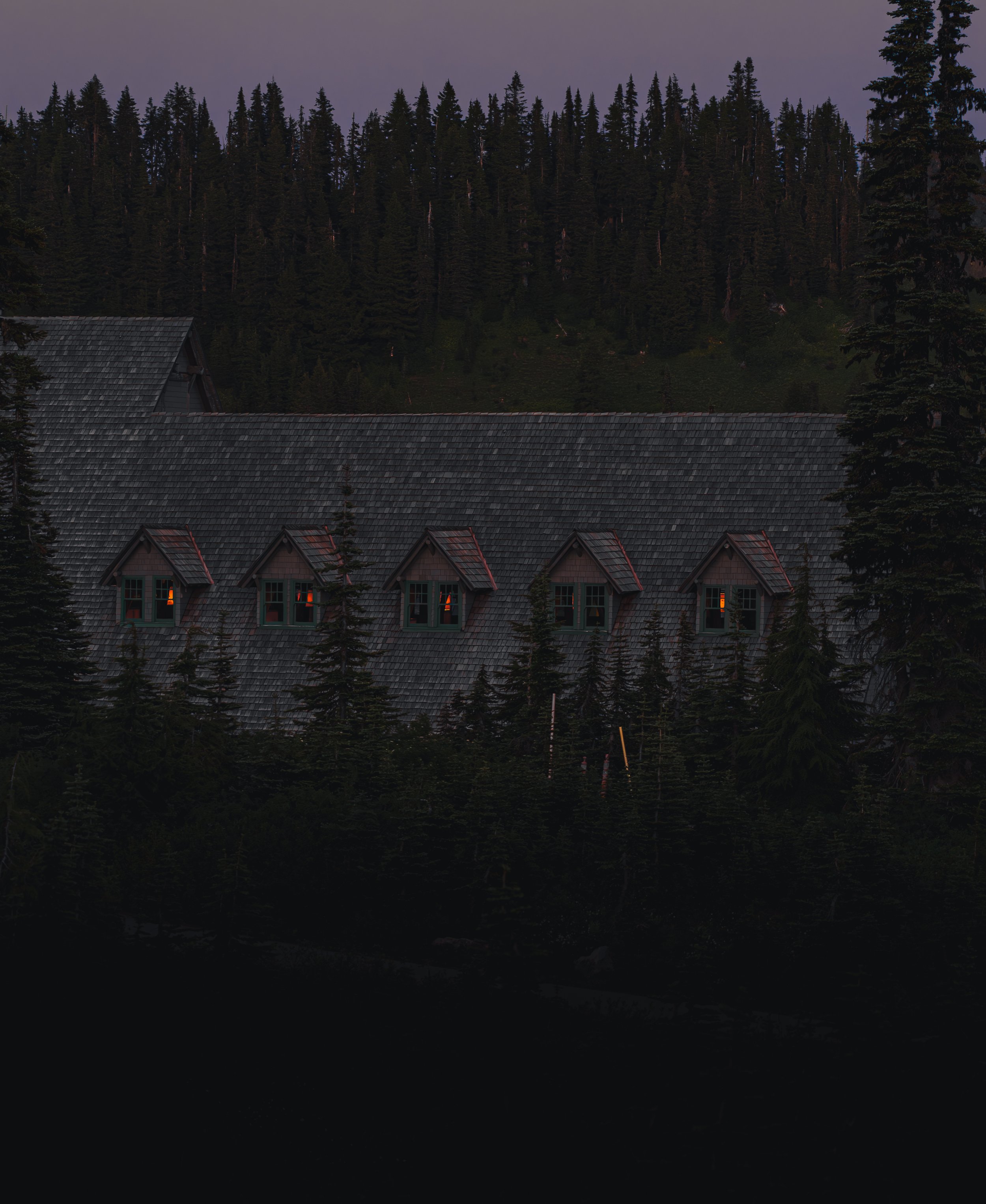 Glowing dormer windows on the historic Paradise Inn roofline at dusk in Mount Rainier National Park.
Warm light spills from the dormer windows of the historic Paradise Inn, offering a cozy contrast to the moody, dark evergreen forest of Mount Rainier