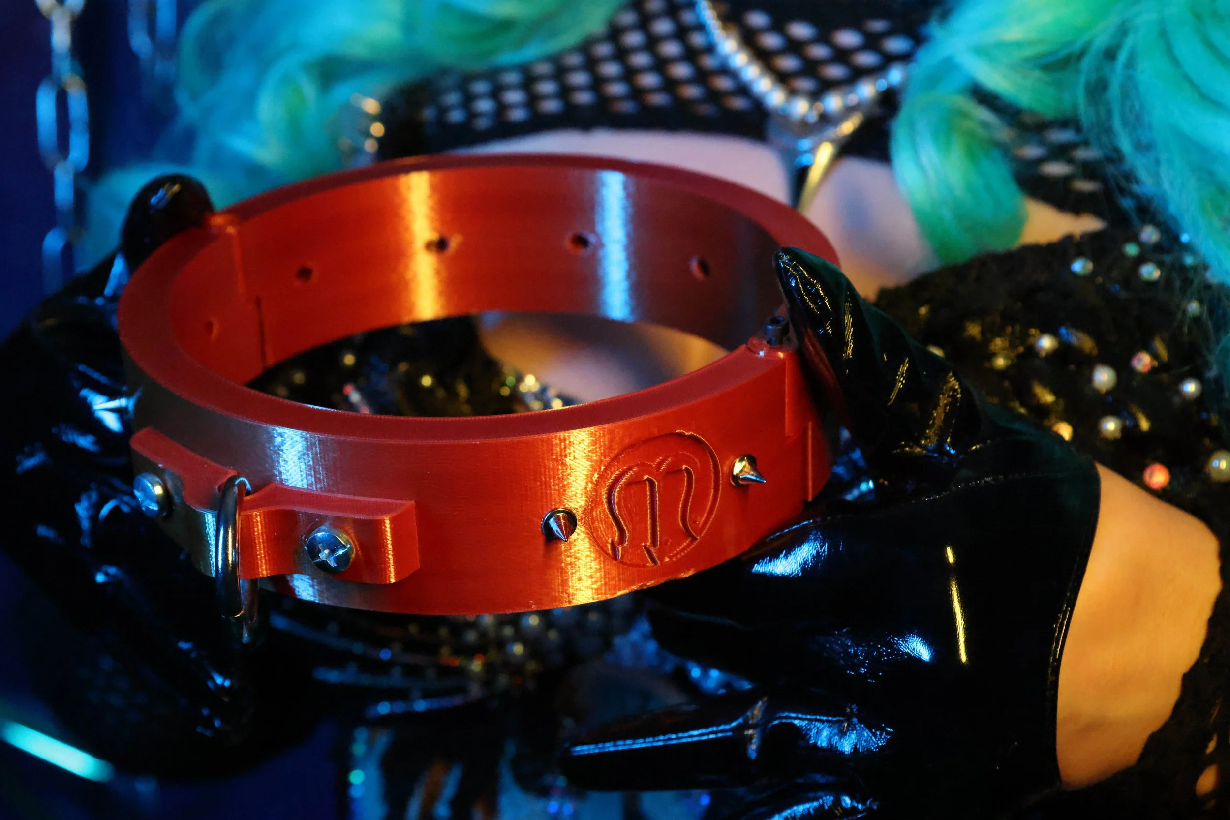 MerDomina holds a copper custom logo collar in PVC-gloved hands and turquoise hair