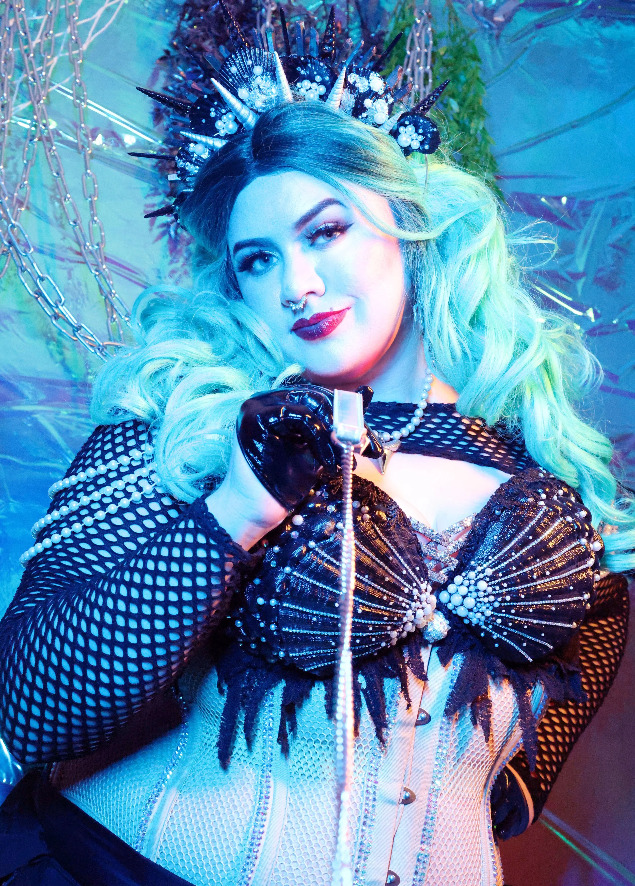 MerDomina looks teasingly at the viewer and pulls a leash in turquoise hair and a sparkly black mermaid burlesque-inspired costume
