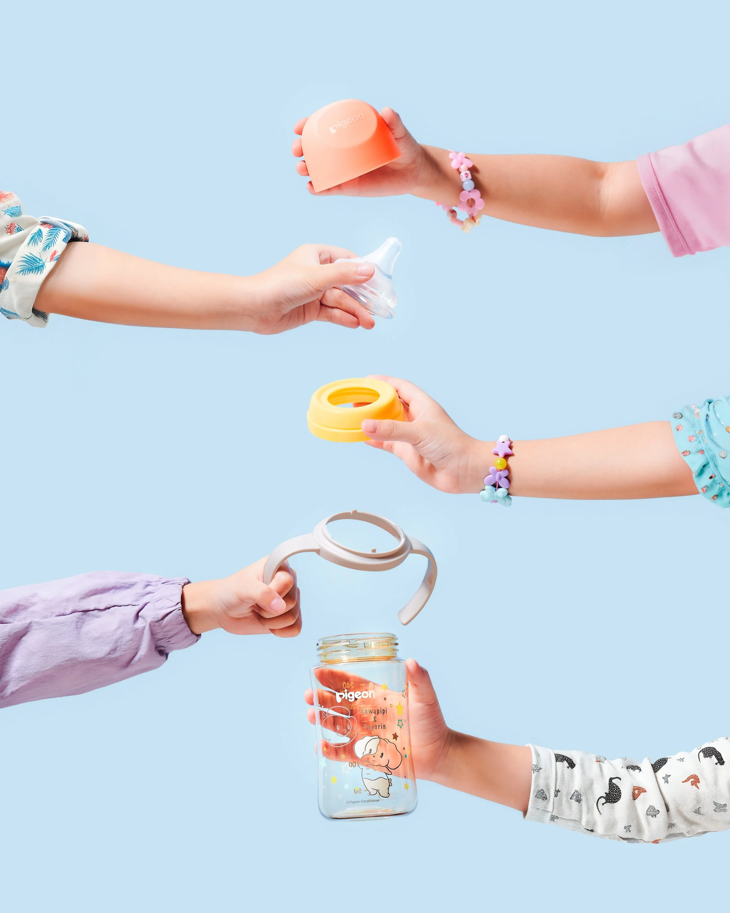 Multiple children holding various baby feeding accessories including a baby bottle, pacifier, and sippy cups against a light blue background.