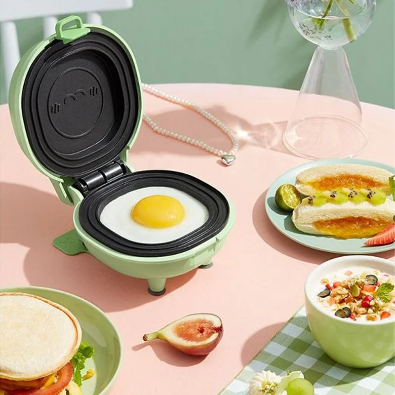 A mini breakfast setup with a breakfast sandwich, salad, a fried egg in a small appliance, a fig, and a bowl of cereal on a pink table with a green and white checkered cloth, and a glass vase with flowers in the background.