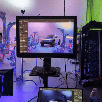 Computer monitor displaying a digital artwork of a futuristic car and abstract landscape with plant-like structures, set in a creative workspace with lighting and equipment.