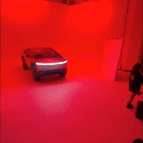 A futuristic, concept car with LED lights is in a red-lit room, with a person standing in the corner.