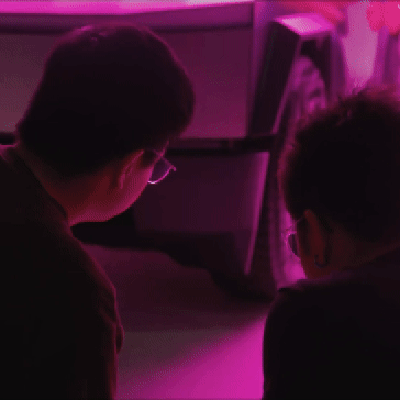 Two people sitting in front of a computer screen with purple lighting.