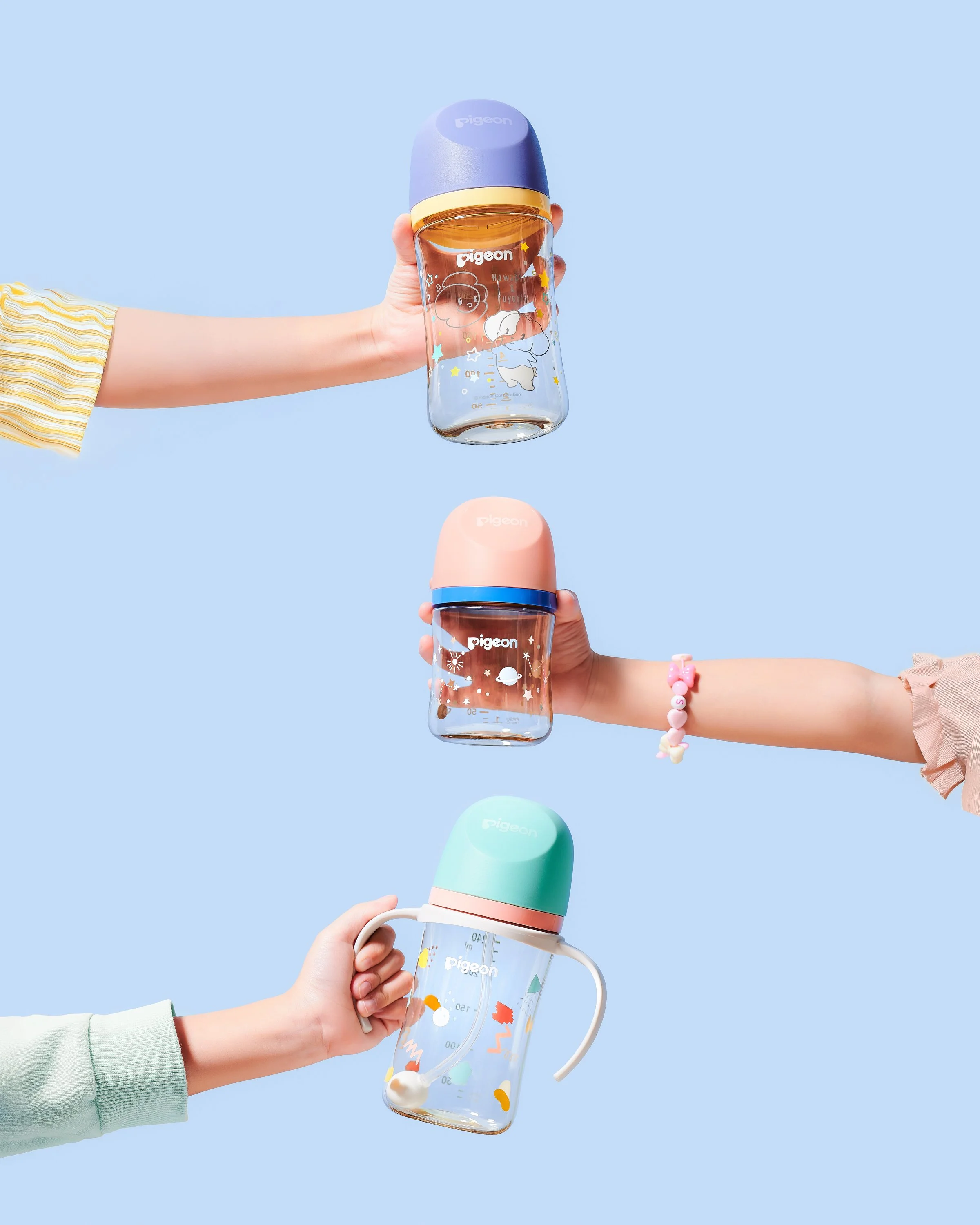 Three children's hands holding colorful baby bottles with cartoon designs against a blue background.
