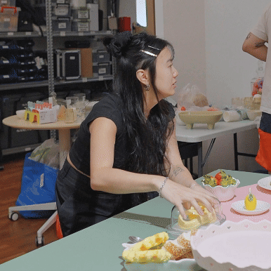 Woman with long black hair and black top decorating a cake at a party table.