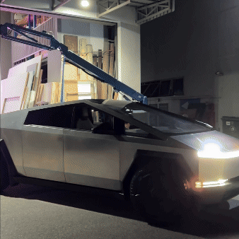 A futuristic, angular vehicle resembling the DeLorean from the Back to the Future movies, with a crane arm extending over it, set in an indoor space with bookshelves and display items in the background.