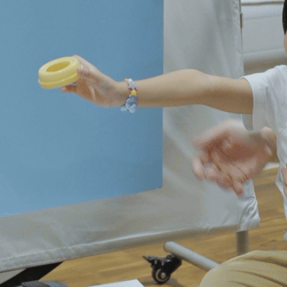 A person holding a yellow tape roll with outstretched arm in a room with blue wall and wooden floor.