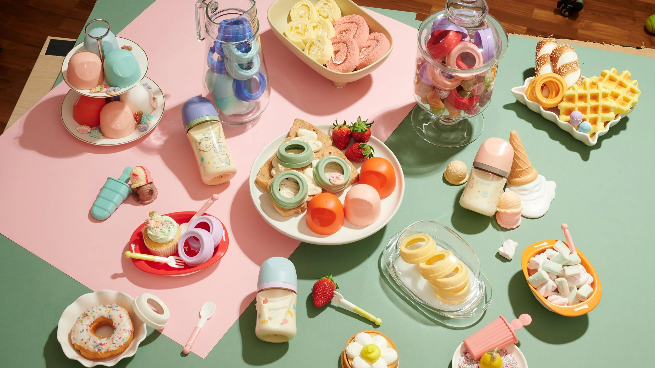 Assorted colorful miniature plastic desserts and food toys on pastel-colored table mats.