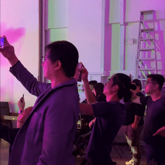 People taking selfies and dancing at a lively indoor event with purple lighting.
