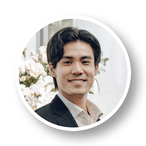 A man in a suit smiling, with white flowers in the background.