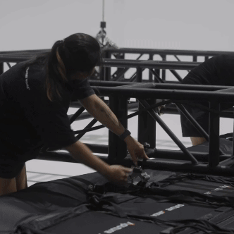 People setting up stage equipment, handling black fabric or equipment on a stage framework.