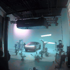 Studio with a car, robotic arms, and filming equipment, lit with neon and studio lights