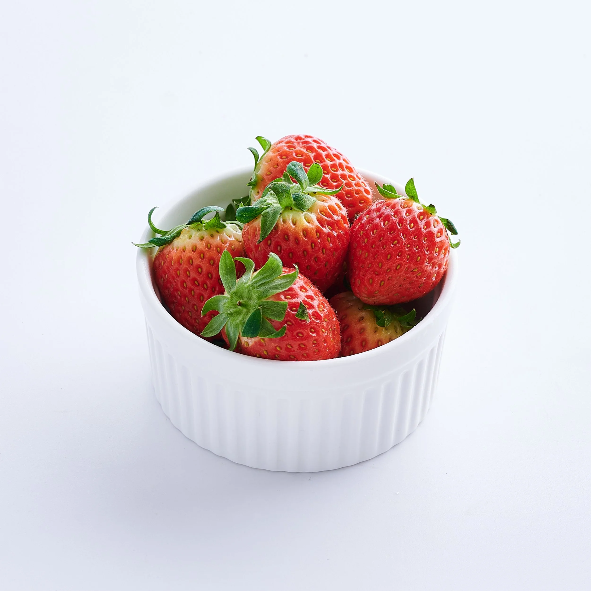 Fresh strawberries in a white ceramic bowl on a white background.