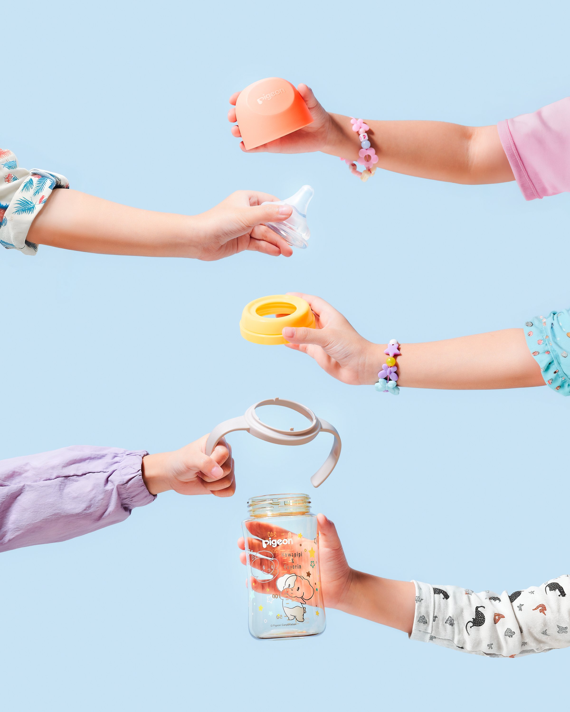 Children's hands holding baby bottles, bottle caps, and a baby bottle with a cartoon design, against a light blue background.