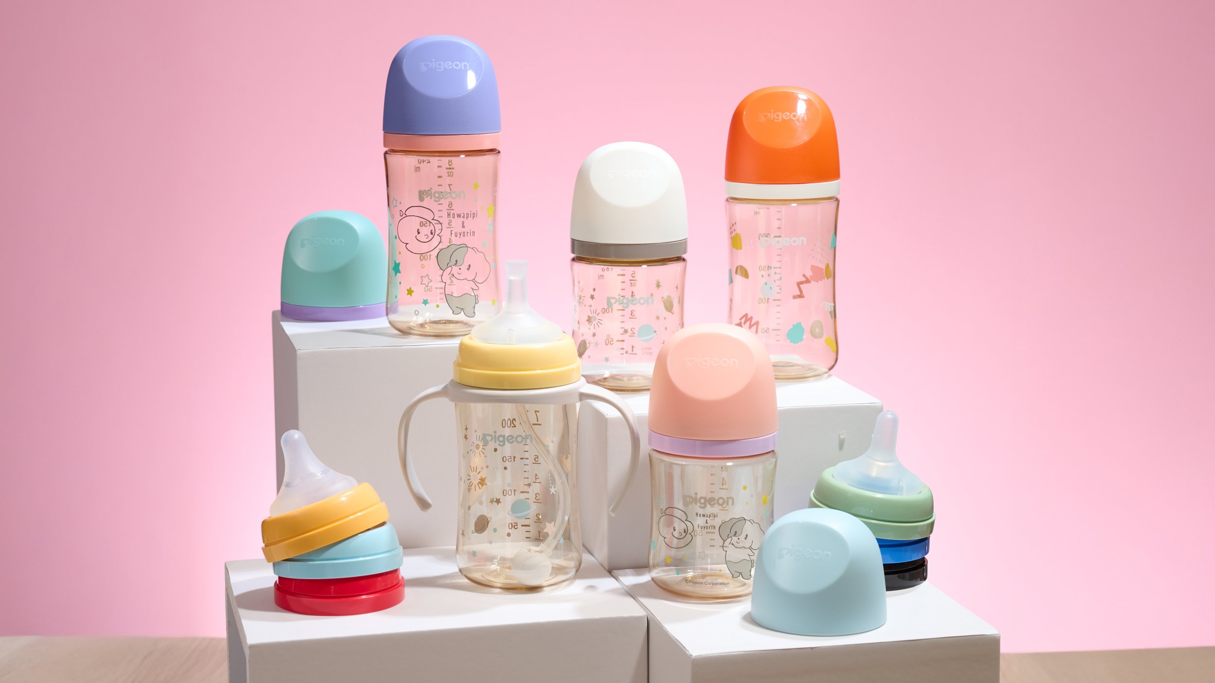 A collection of baby bottles and sippy cups in pastel colors, displayed on white platforms against a pink background.